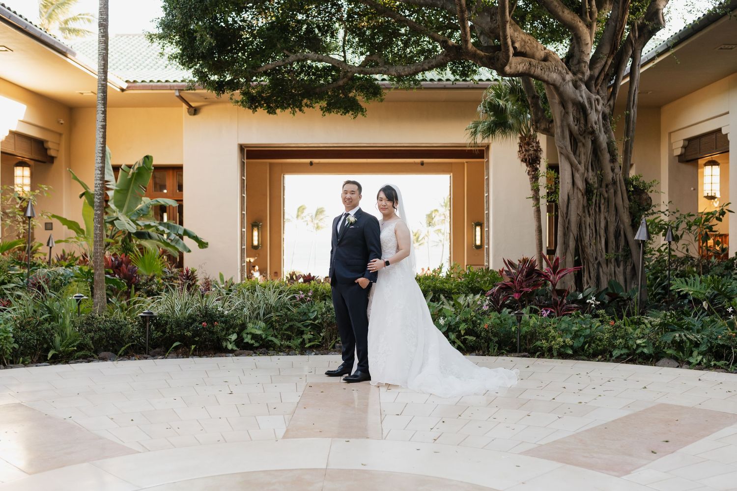 Wedding couple poses in an elegant outdoor courtyard with tropical landscaping.