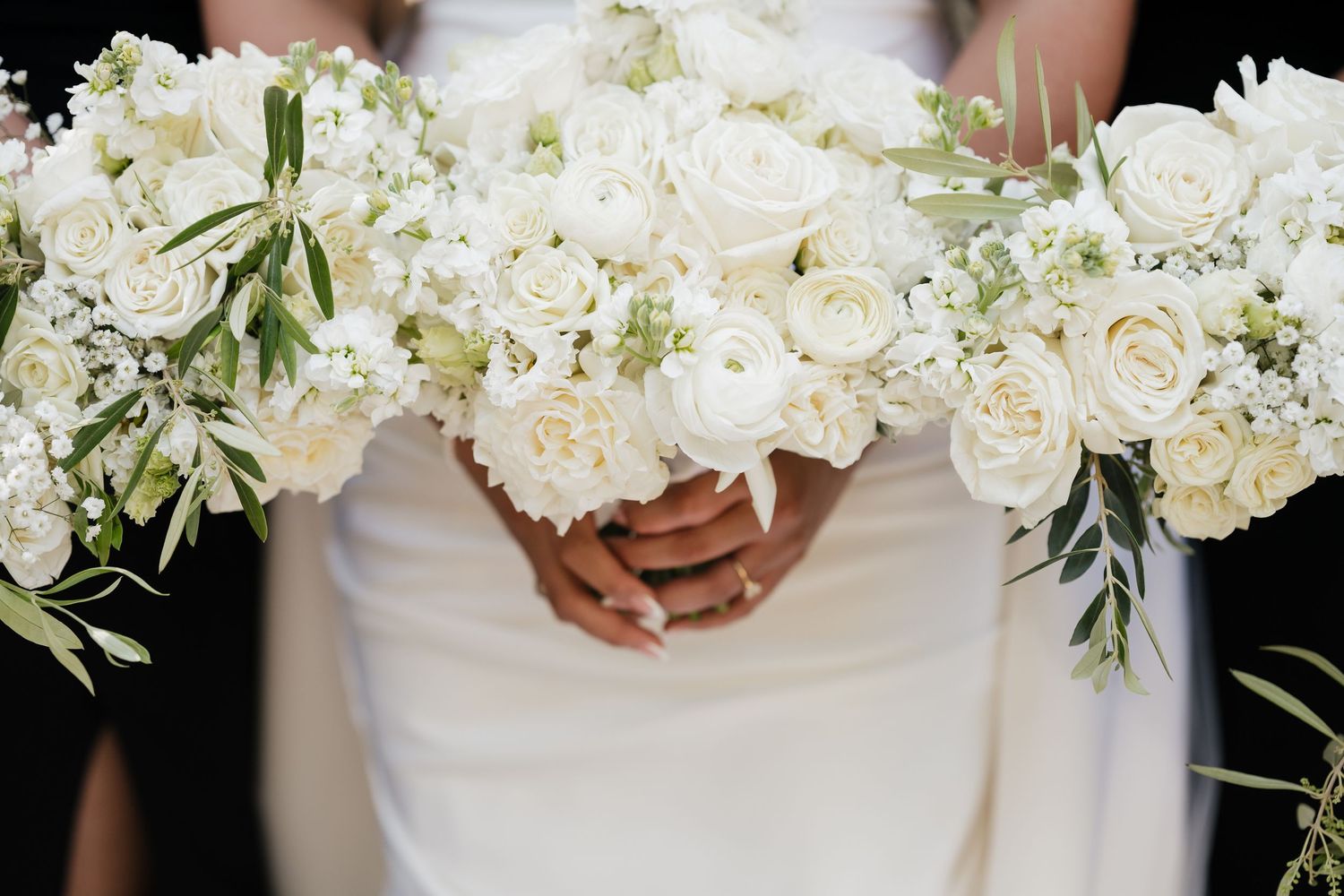 Bride holding elegant white rose and ranunculus wedding bouquet with greenery, flanked by matching bridesmaid bouquets.