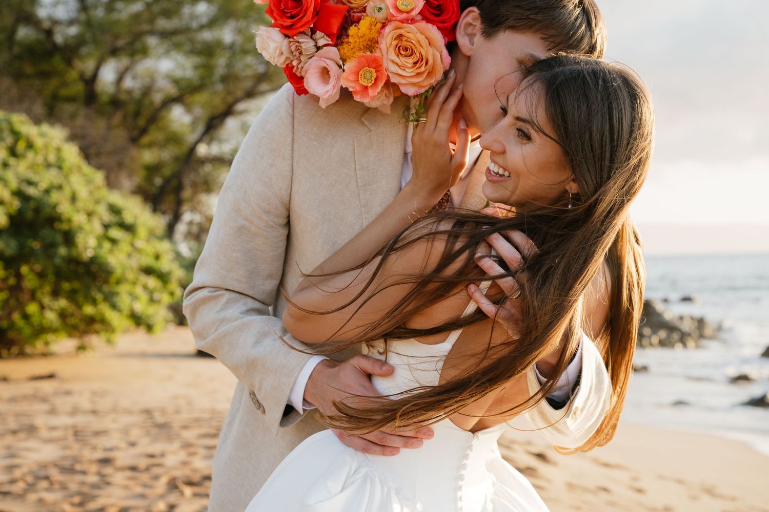 A romantic couple shares tender moments at sunset on a tropical beach with orange and red flowers in the background.