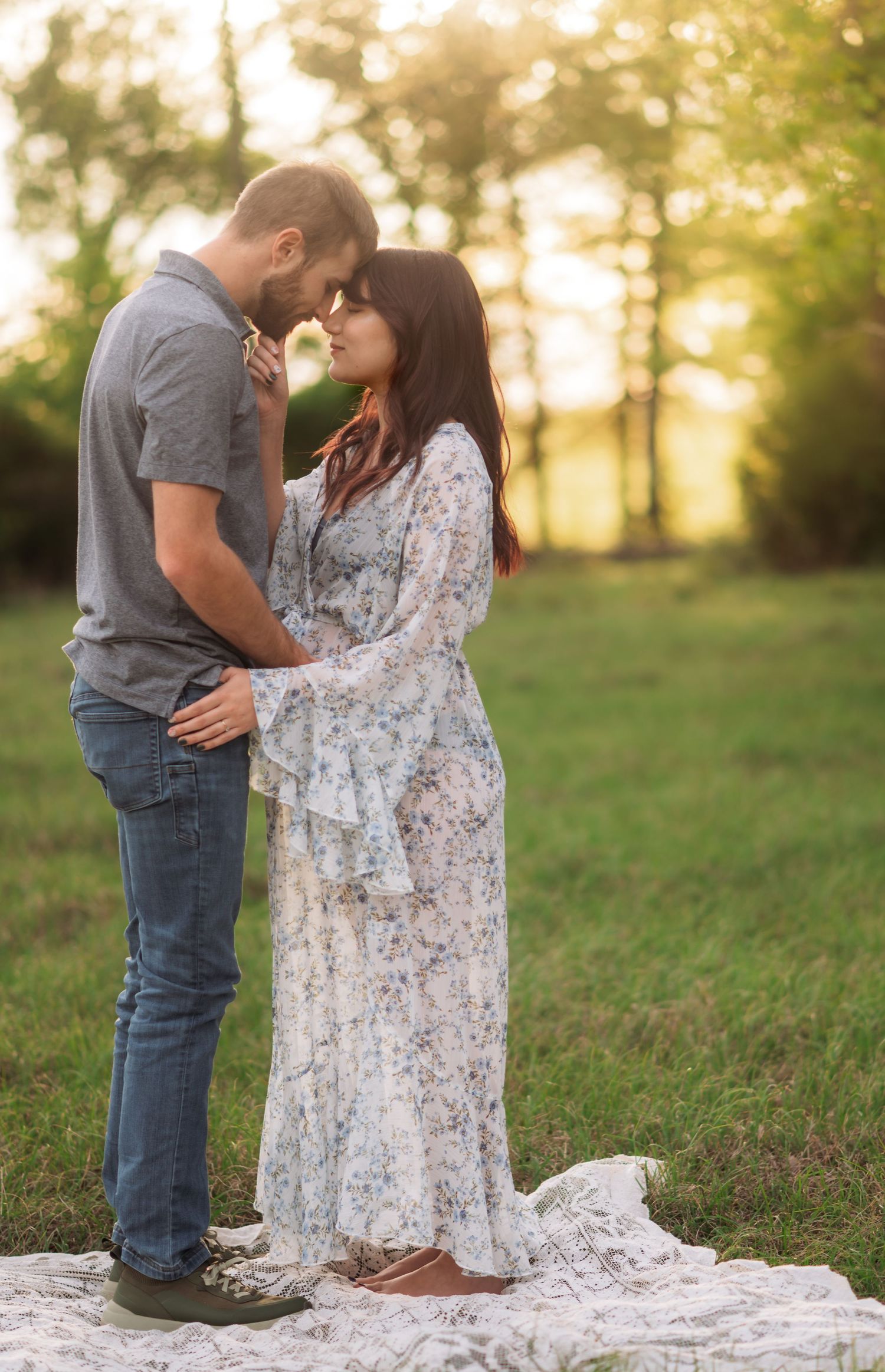 A couple shares a romantic moment in a sunlit field, the woman in a floral maxi dress touching foreheads with her partner.