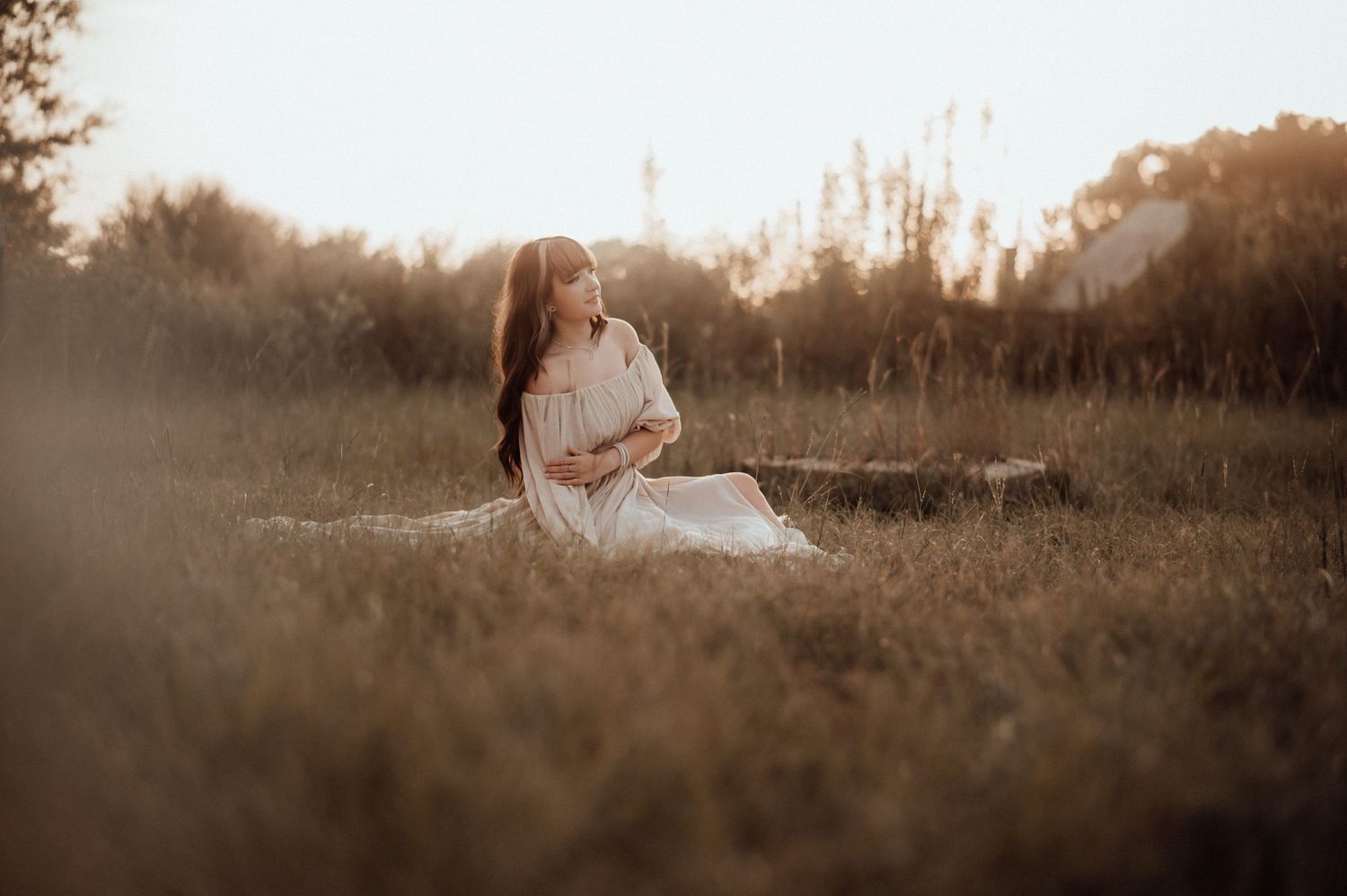 Woman in white dress sitting peacefully in golden field at sunset.