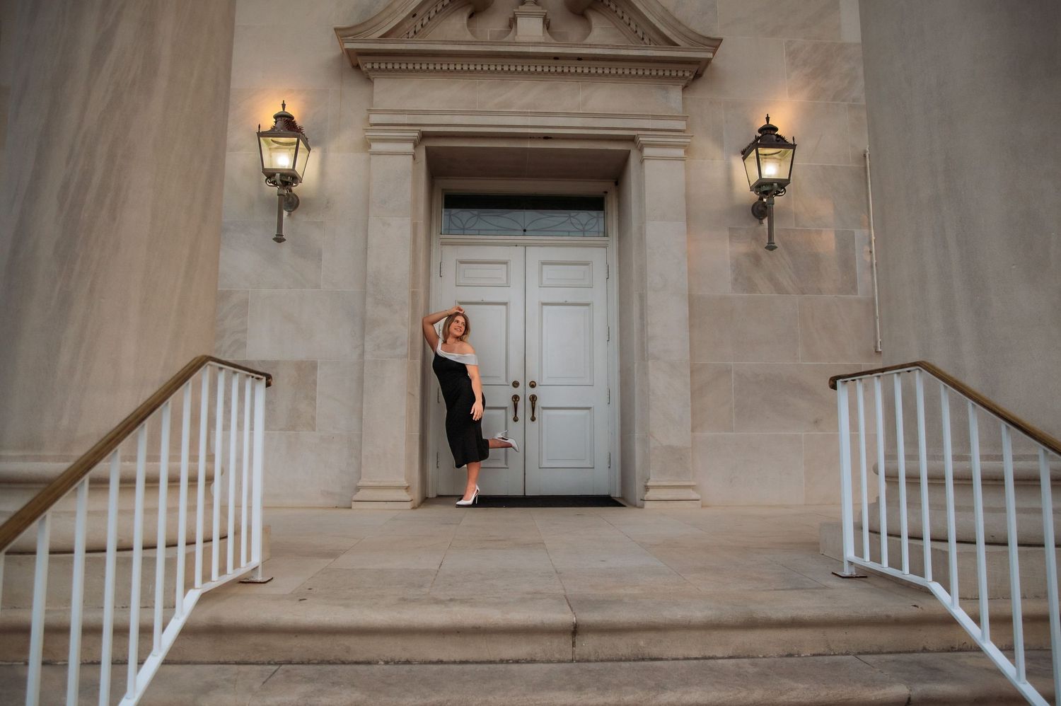 Woman in black dress posing at grand entrance with stone steps and lanterns.