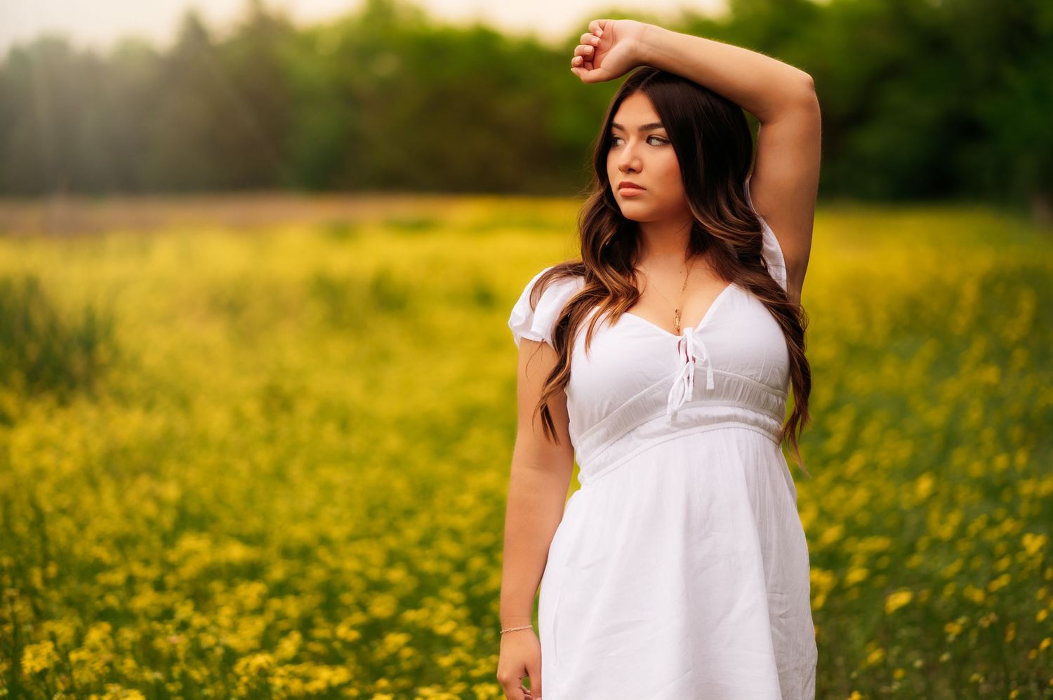Young woman in white dress standing gracefully in a vibrant yellow wildflower field during golden hour.