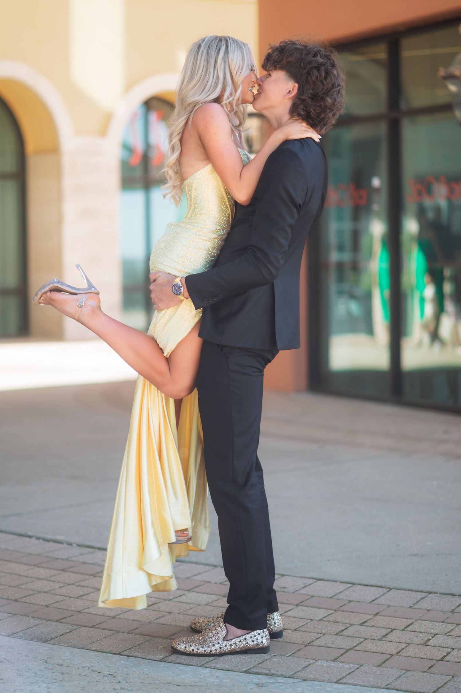 Young couple in formal wear sharing a romantic moment outdoors, woman in yellow gown lifted by man in black suit.
