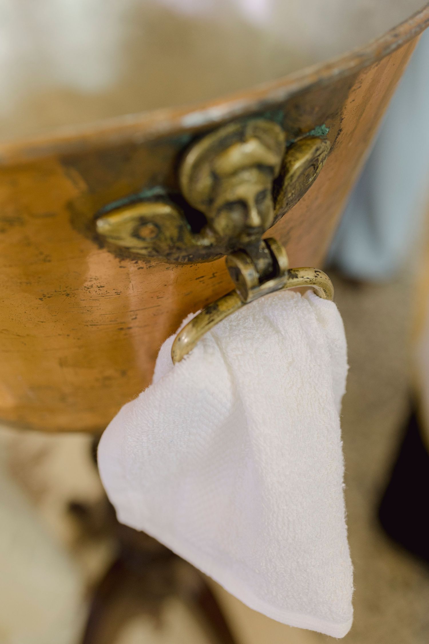 Ornate copper basin with brass cherub ring holding a white cloth towel, vintage decorative washbowl.