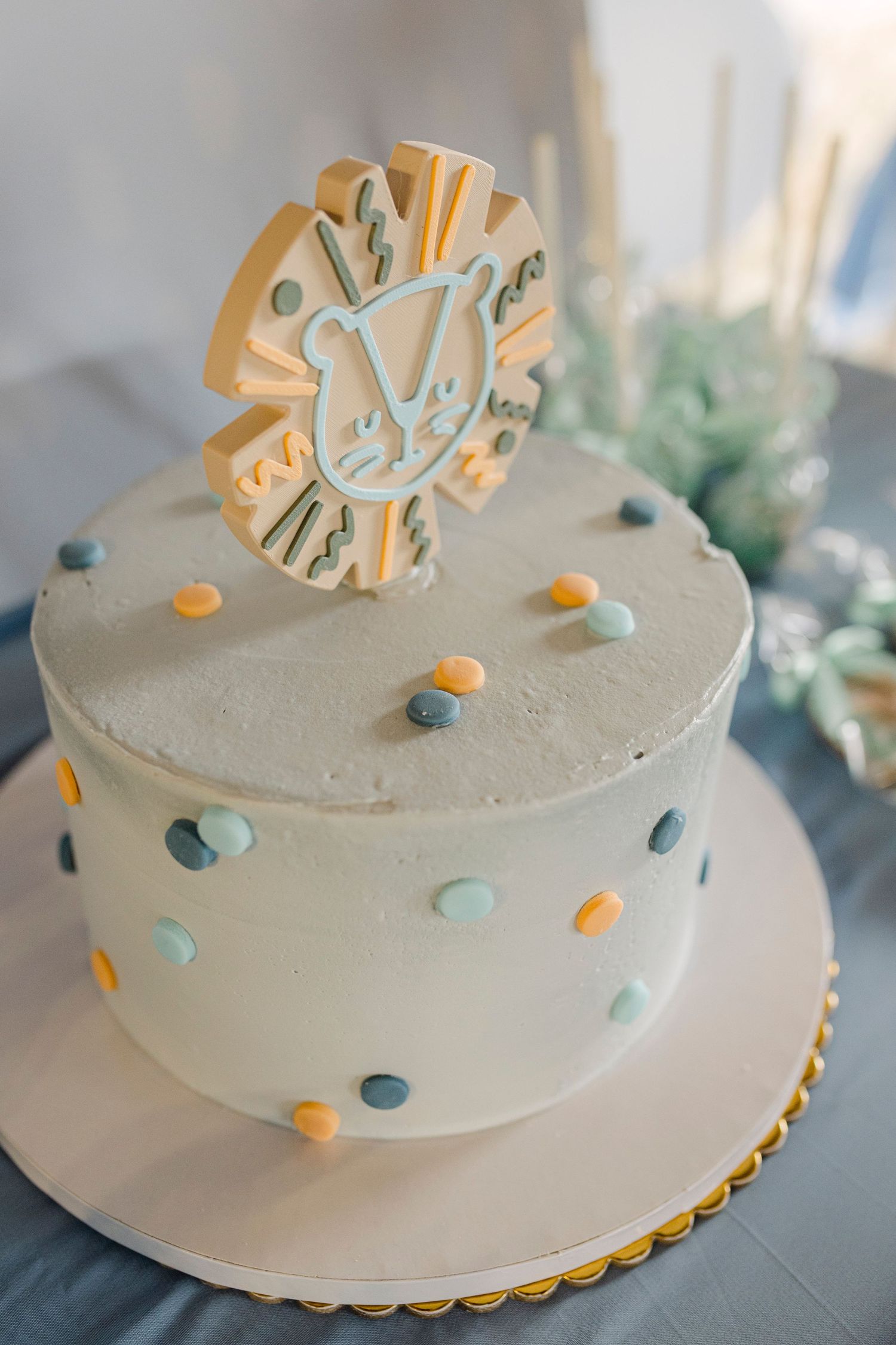 White birthday cake with colorful polka dots and a lion topper decoration on a table.