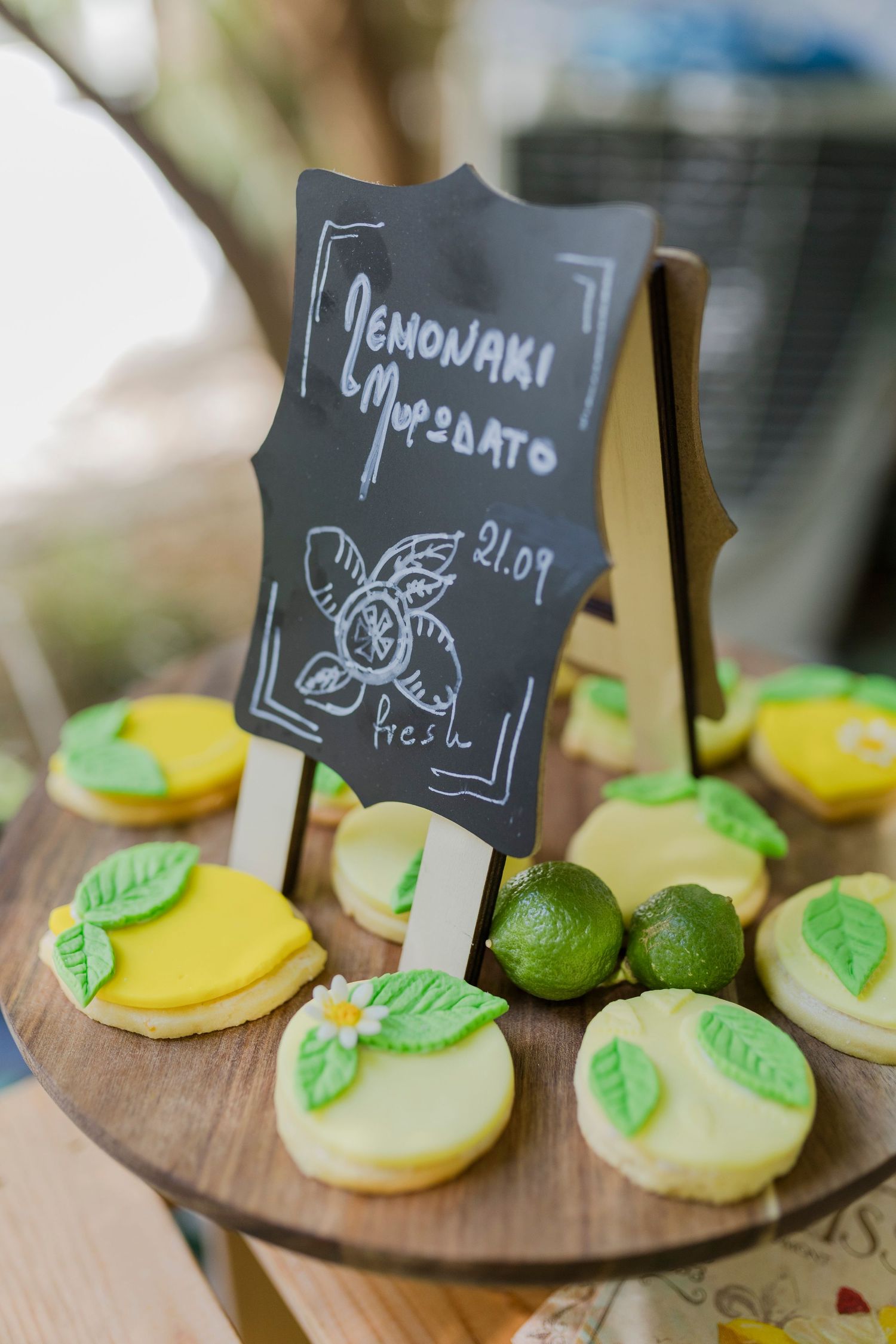 Lemon-themed decorated cookies and limes displayed on wooden stand with chalkboard sign at wedding.