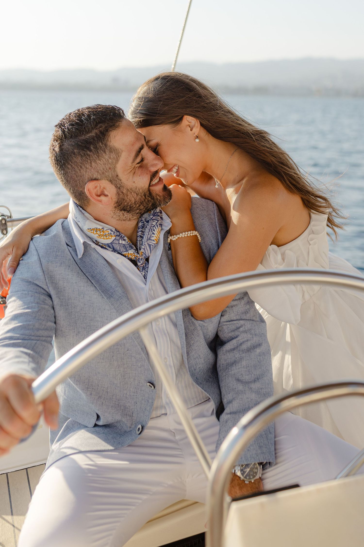 Romantic couple sharing a kiss on a sailboat deck with blue water in background.