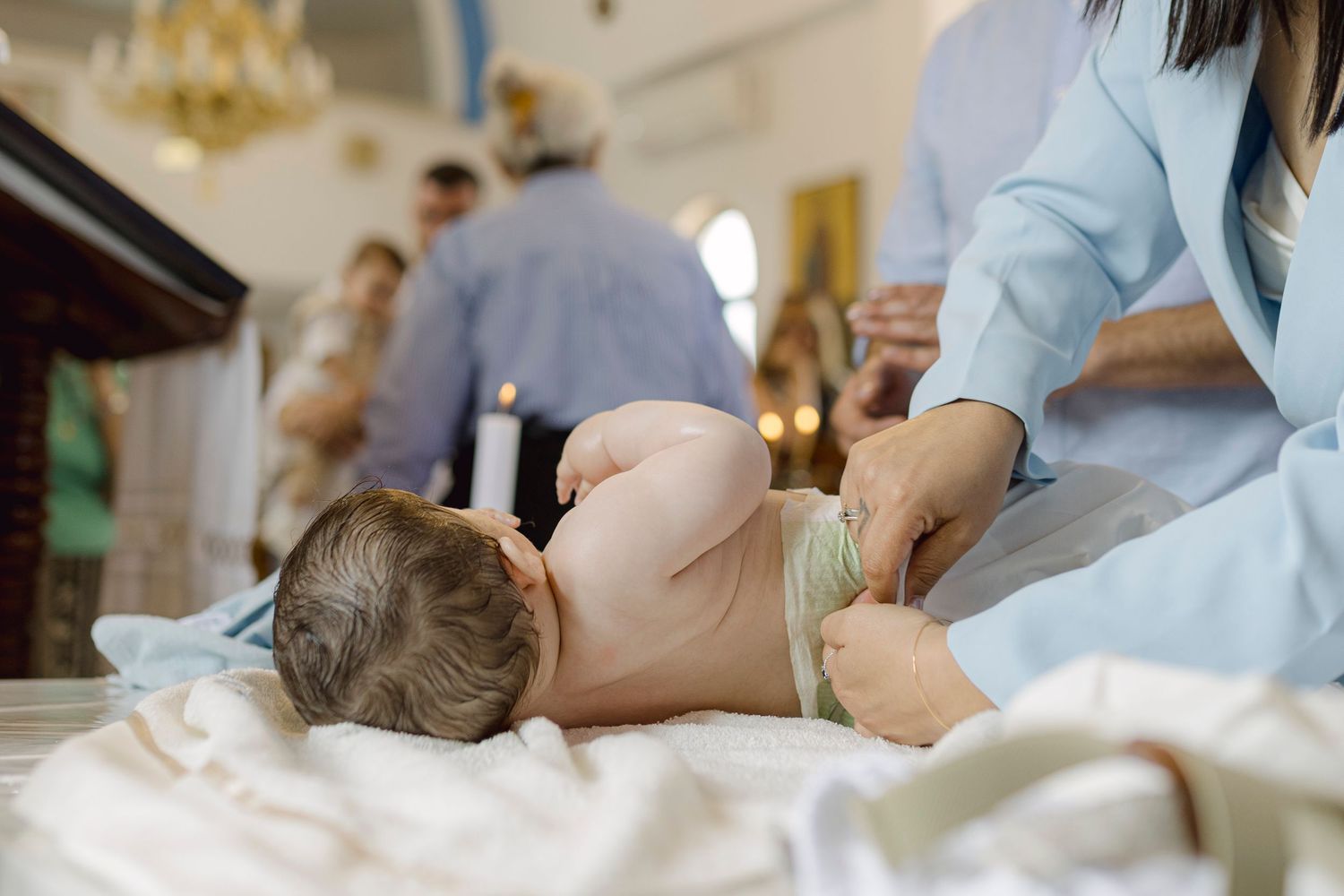 A newborn baby lying on a white cloth during a baptism ceremony in a church.
