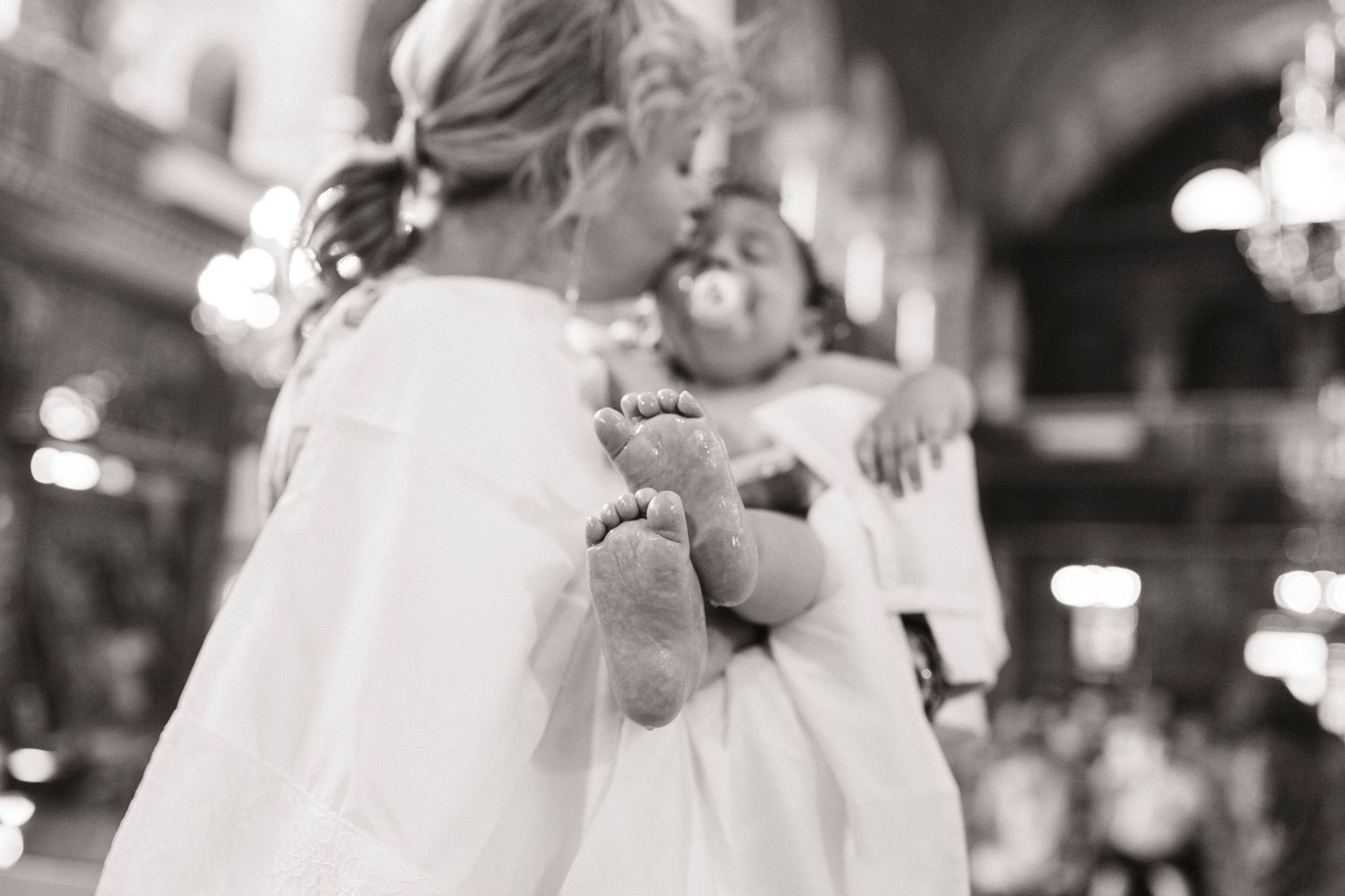 Black and white photo of two young children in white baptismal gowns, one holding a baby during a church ceremony.