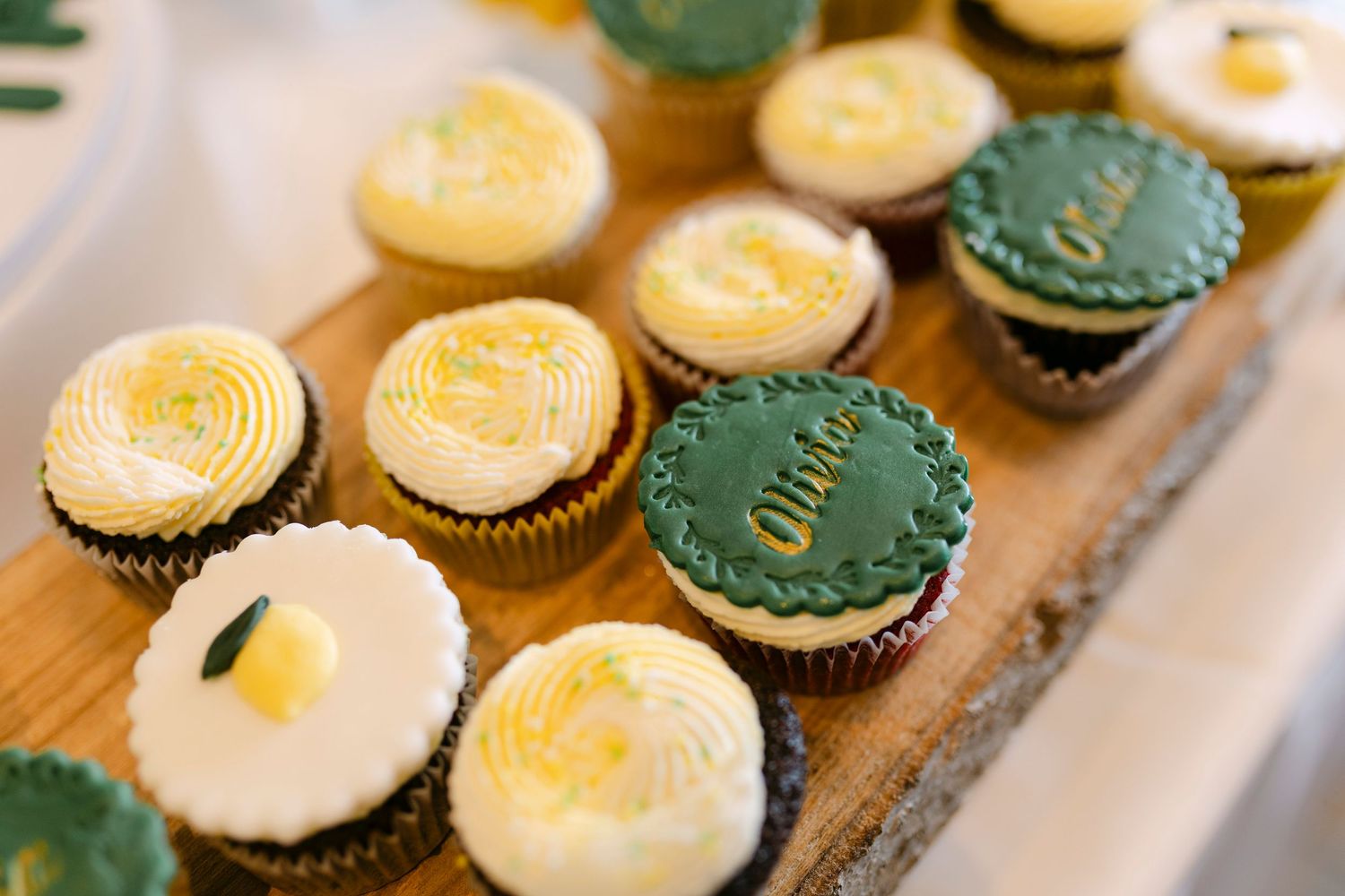 Assorted lemon and green frosted cupcakes on a wooden board, with decorative fondant toppers at a celebration event.