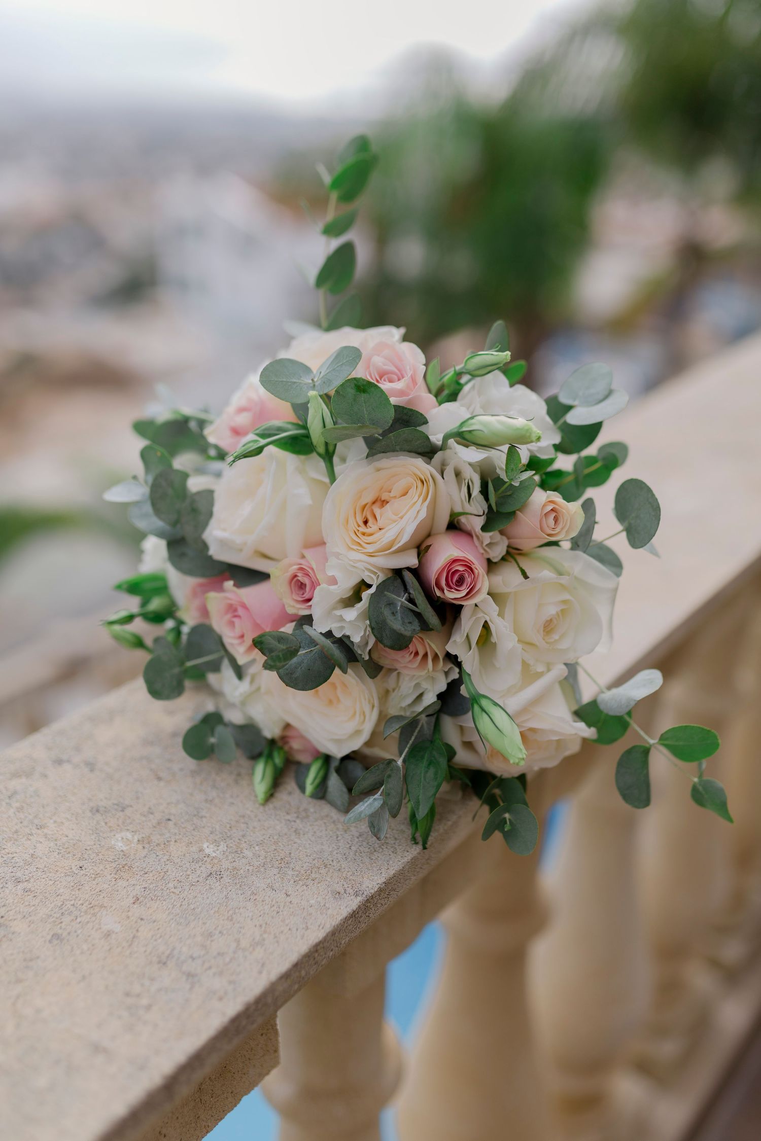 Elegant bridal bouquet of white and pink roses with eucalyptus on a stone balustrade.