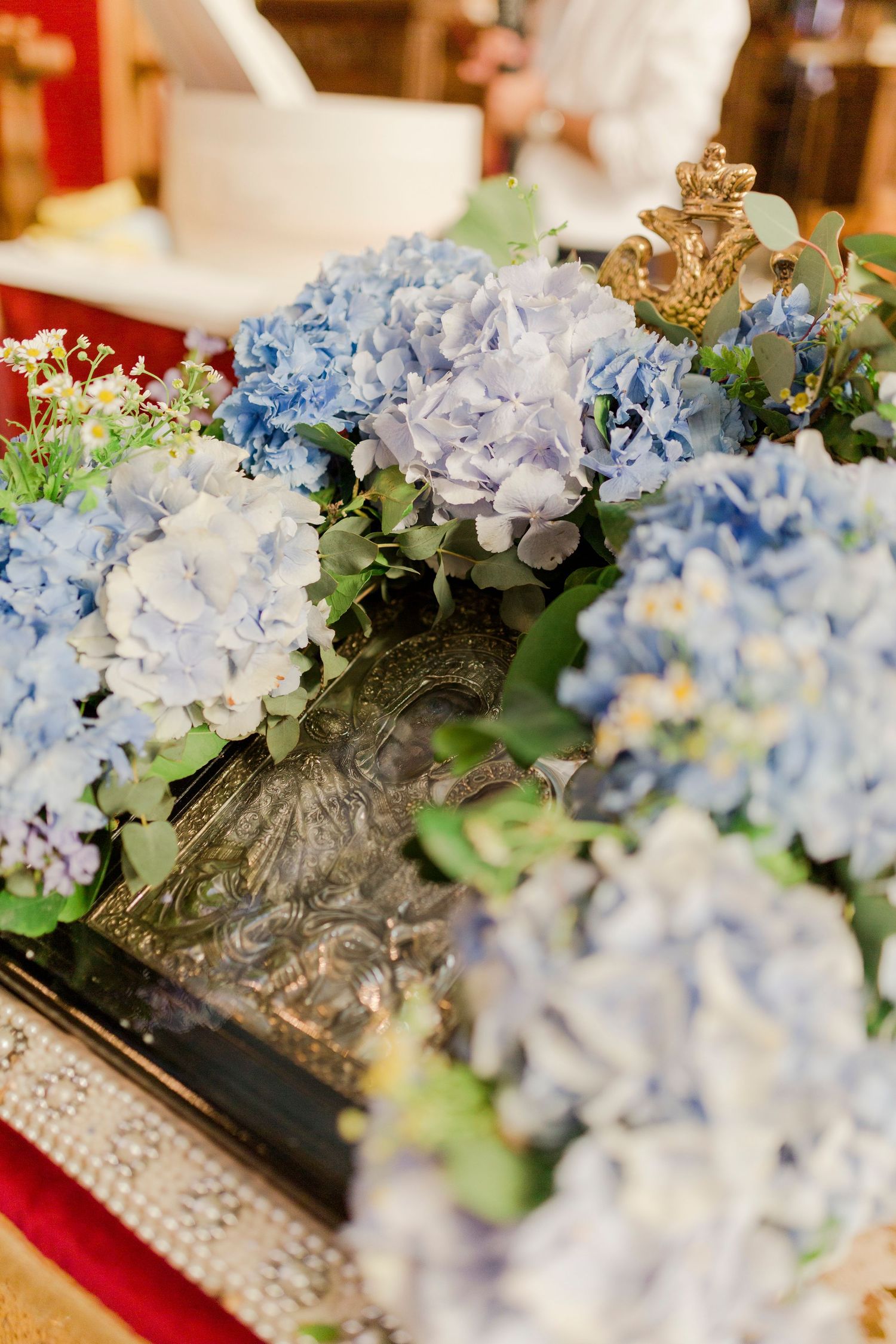 Blue hydrangea flowers arranged around an ornate religious icon on a decorated altar in a church.