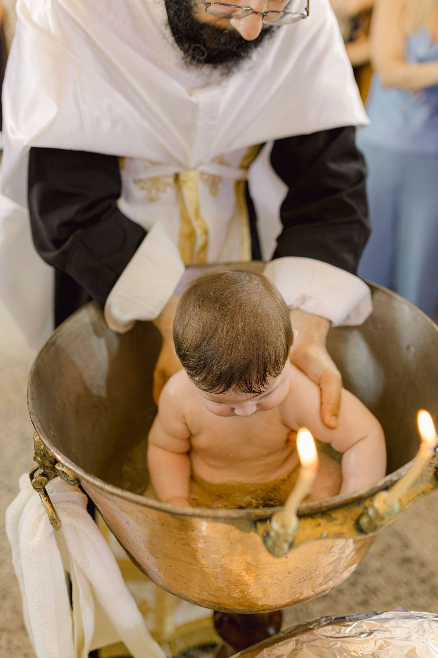 Priest performing a traditional Christian baby baptism ceremony in a golden font.