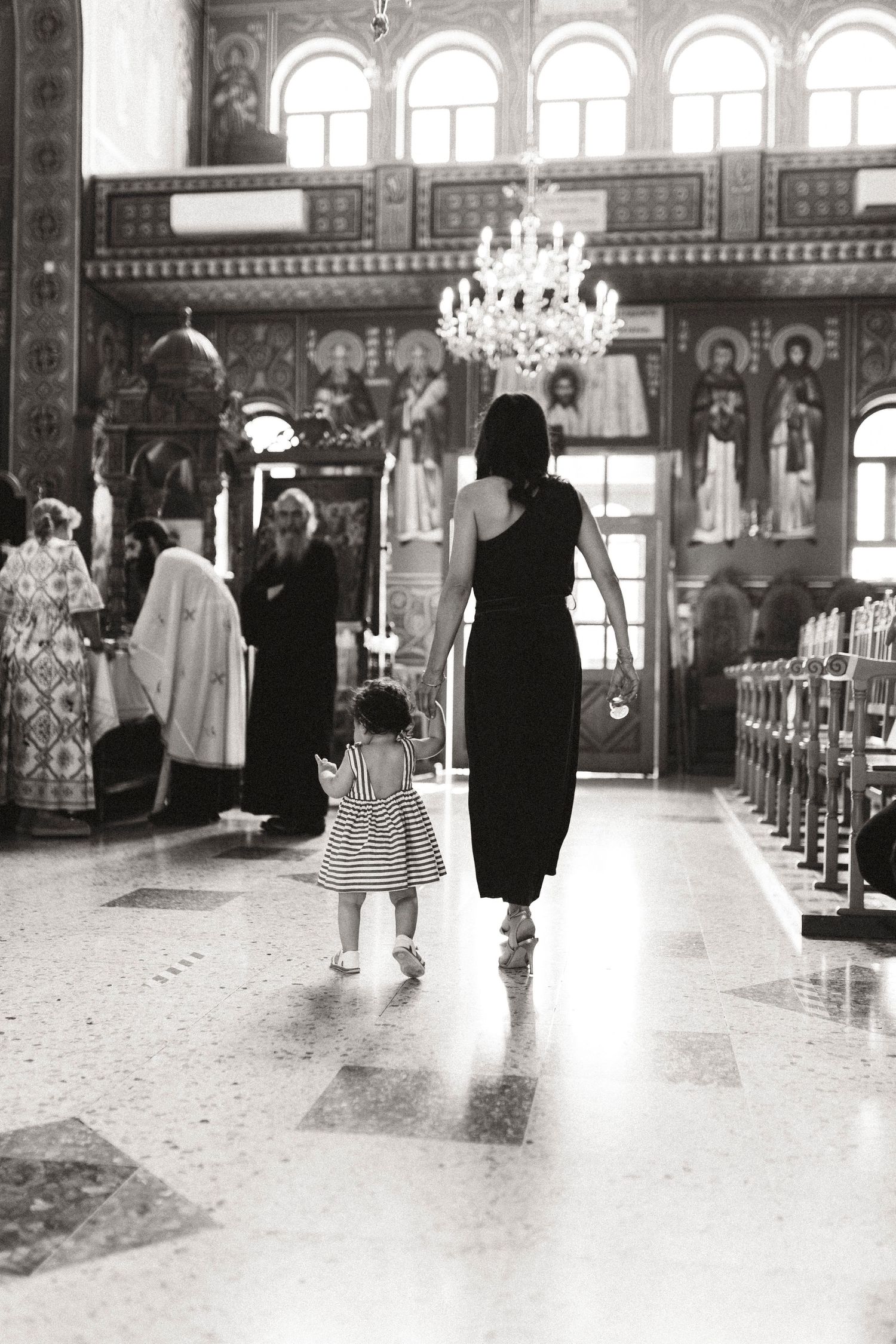 Black and white photo of a woman and child walking through an ornate Orthodox church interior with chandelier.