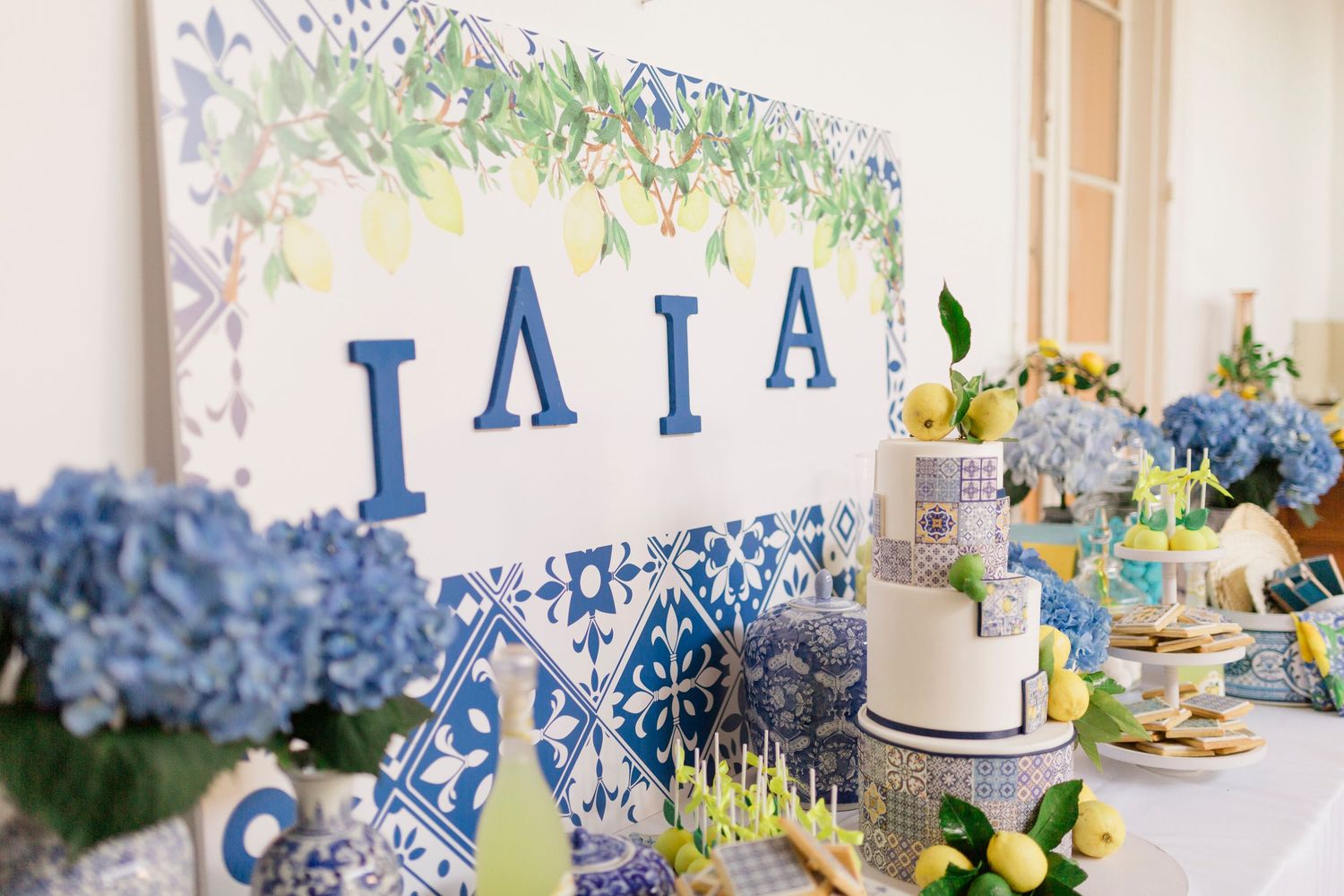 Blue and white tile-themed dessert table with hydrangeas, lemons, and a cake for a Greek-inspired party.