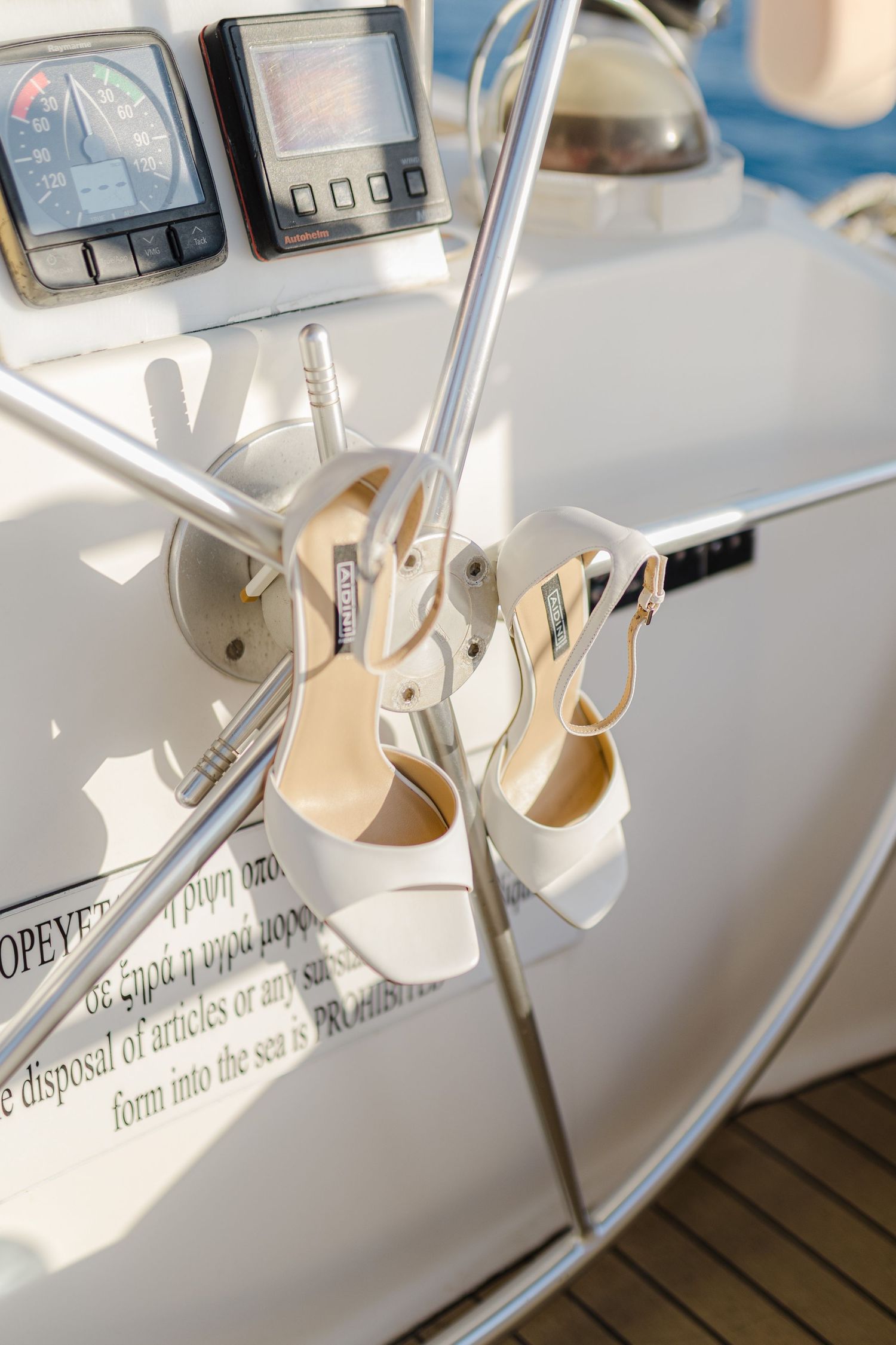 Elegant white heeled sandals hanging on a yacht steering wheel with navigation instruments in background.