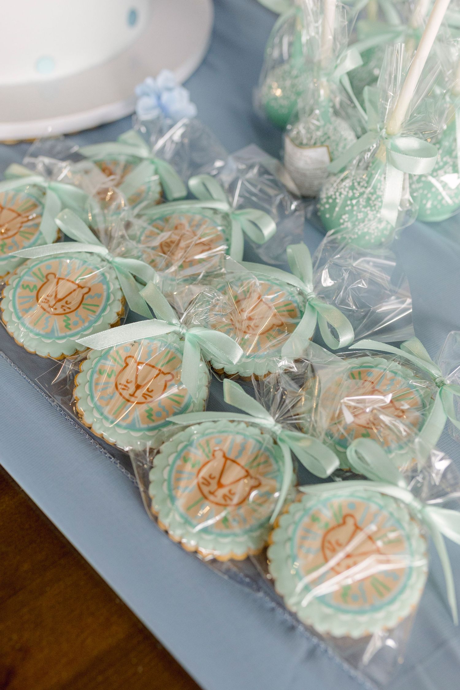 Mint green decorated sugar cookies with bow ties and cake pops on a dessert table for a baby shower.