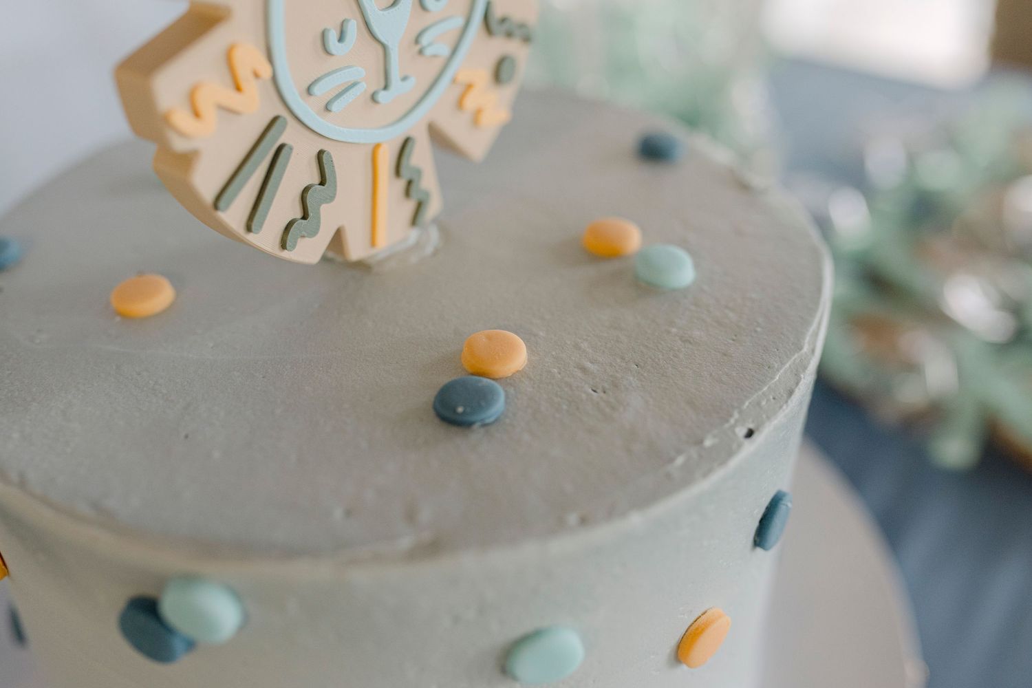 Light blue frosted birthday cake with colorful candy dots and a decorative topper on a white surface.