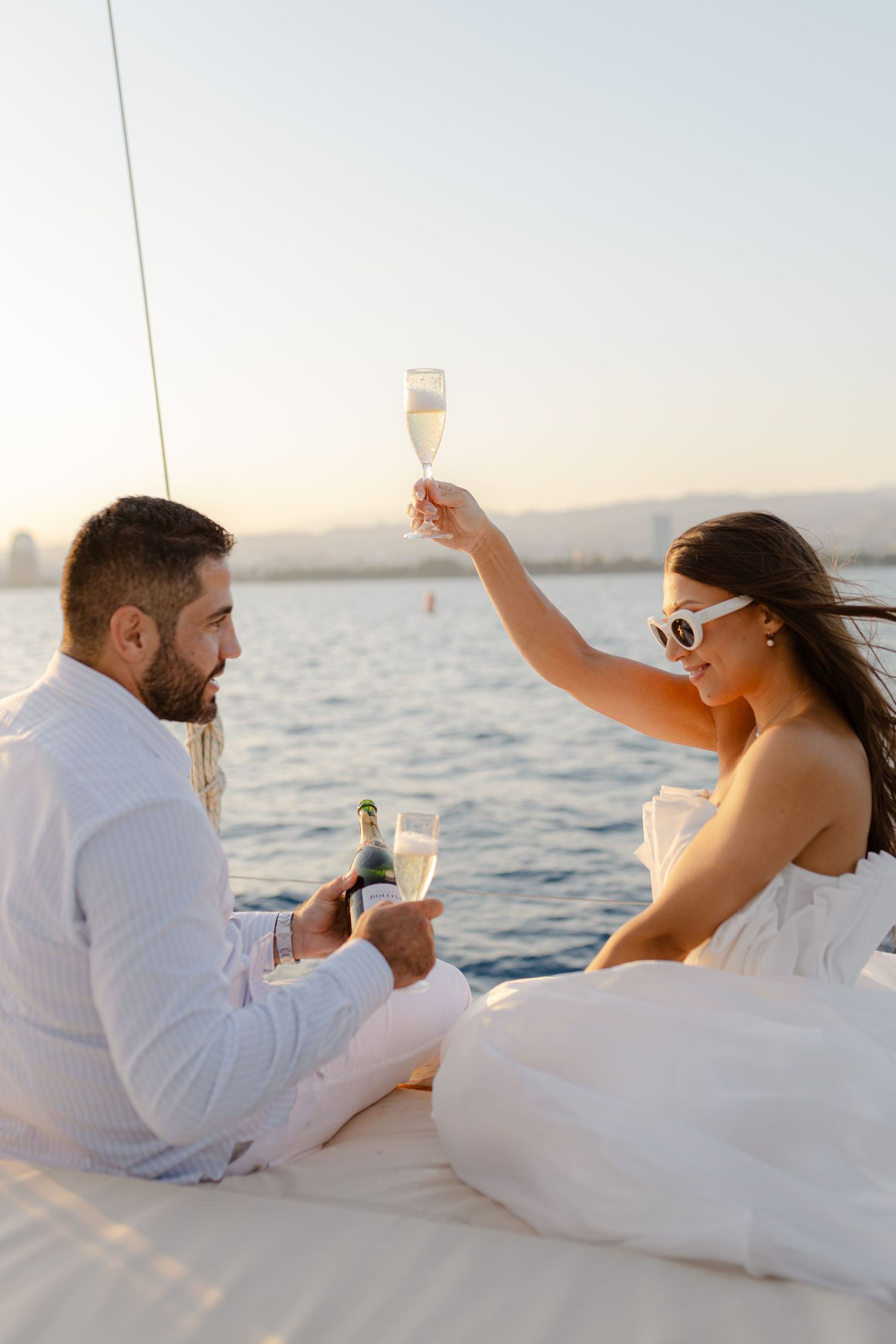 Couple celebrating with champagne glasses on yacht deck at sunset over calm water.