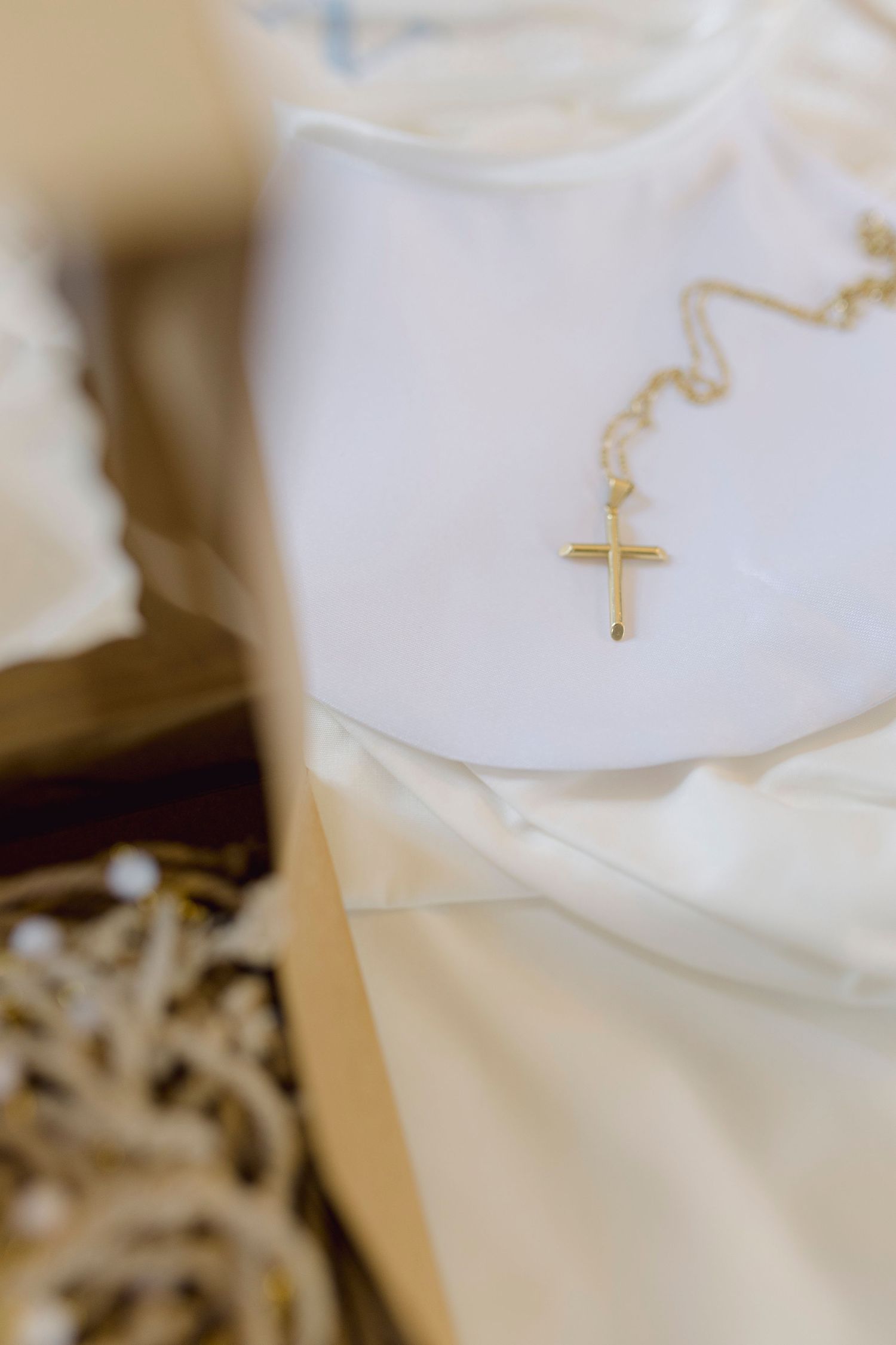 Gold cross necklace on white satin fabric, elegant religious jewelry gift for baptism or wedding.