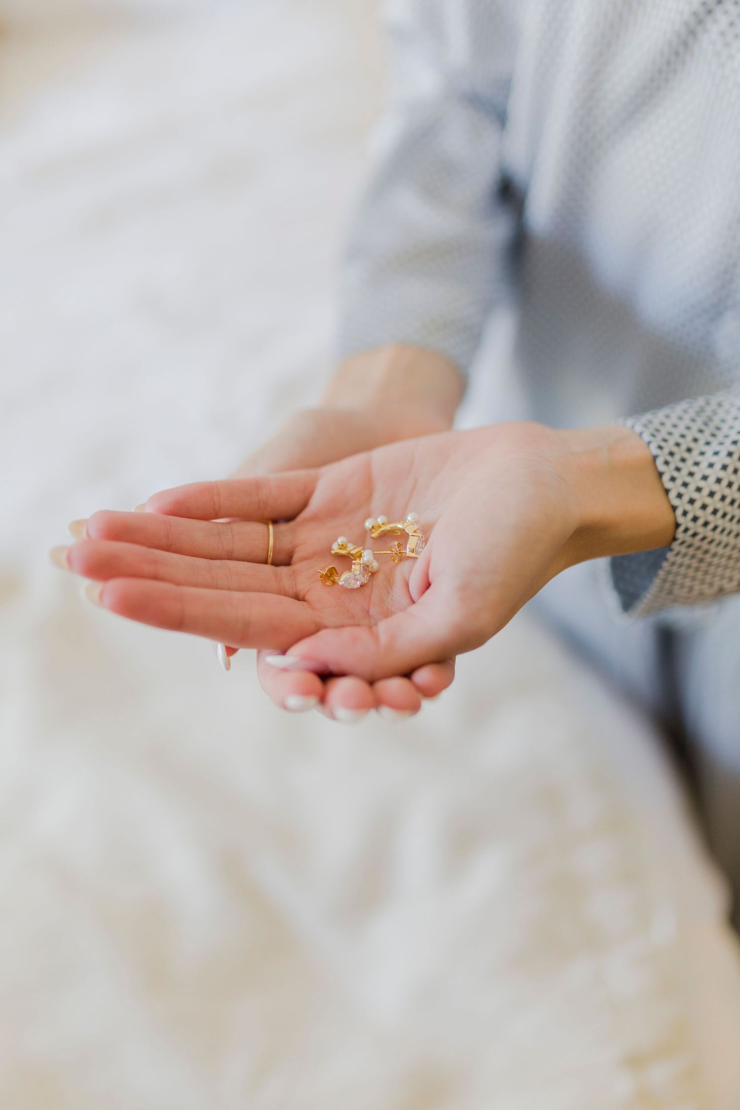 Bride holding delicate gold crystal earrings in her open palm before wedding.