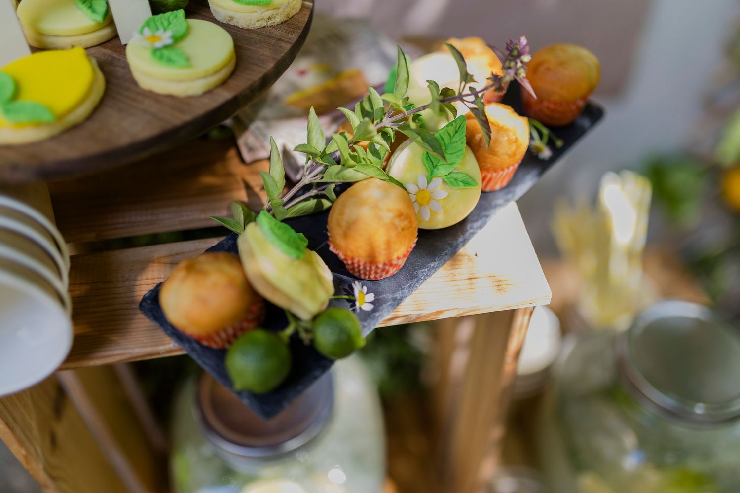 Elegant dessert display featuring lemon muffins garnished with fresh herbs and limes on a rustic wooden tiered stand.