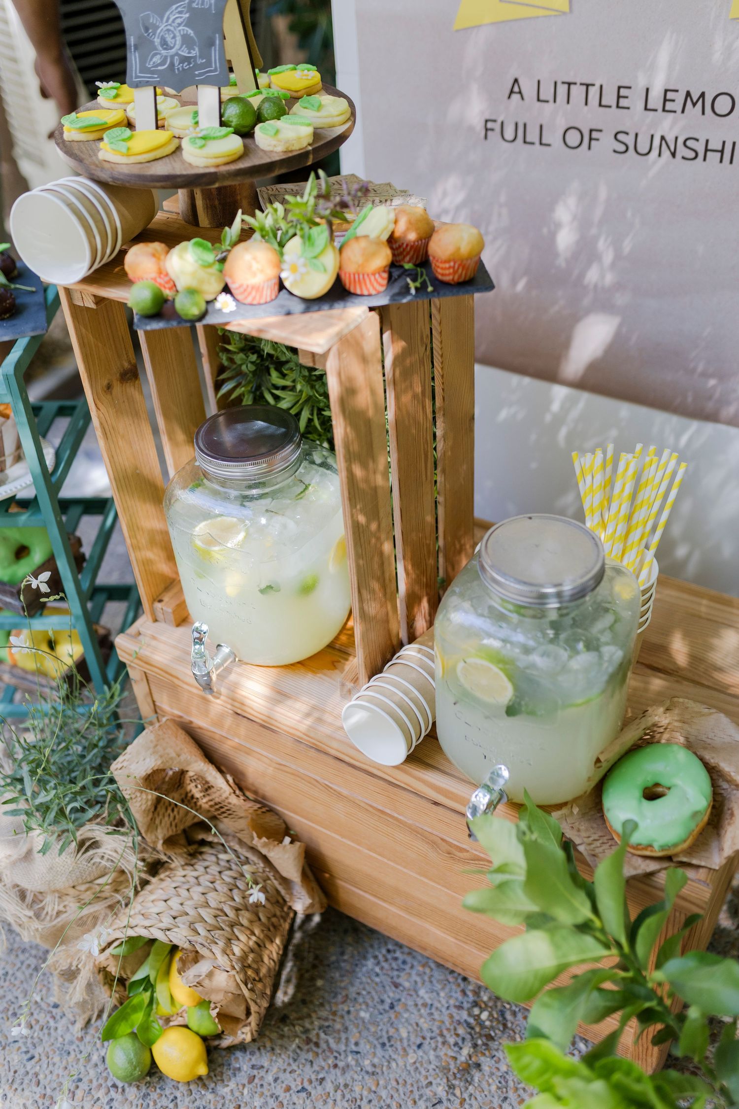 Rustic lemon party dessert table with lemonade dispensers, cookies, and sunshine-themed decor on wooden crates.