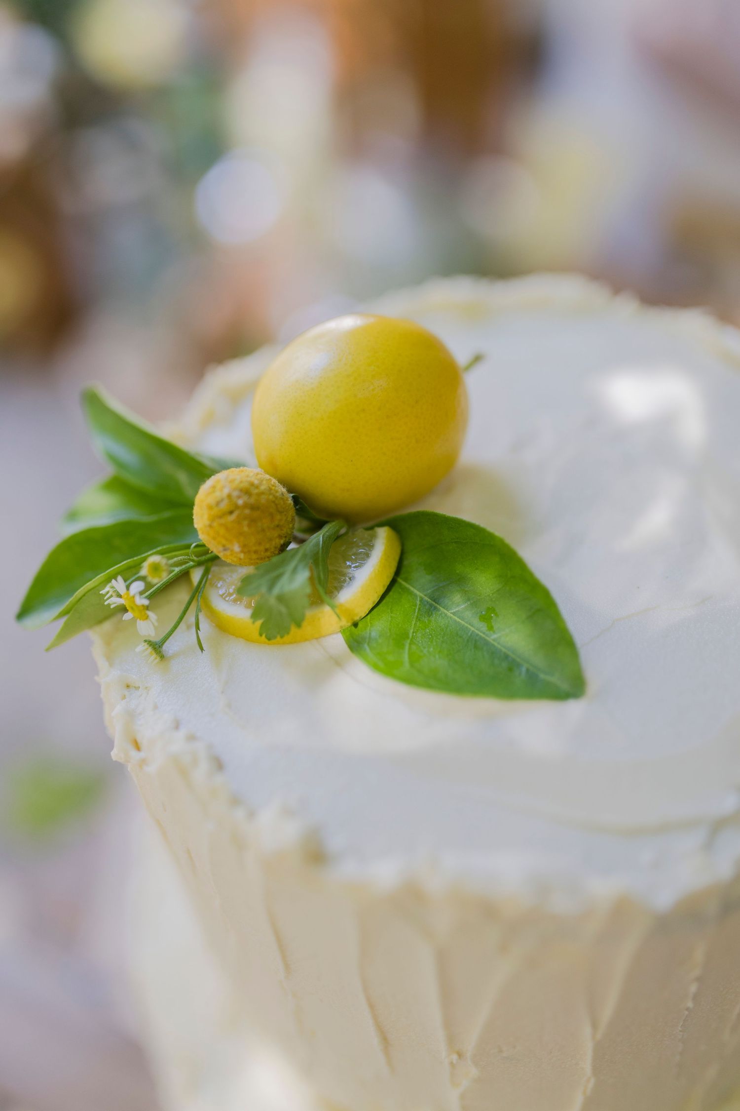 White wedding cake topped with fresh green leaves, yellow lemon slices, and decorative yellow fruit accents.