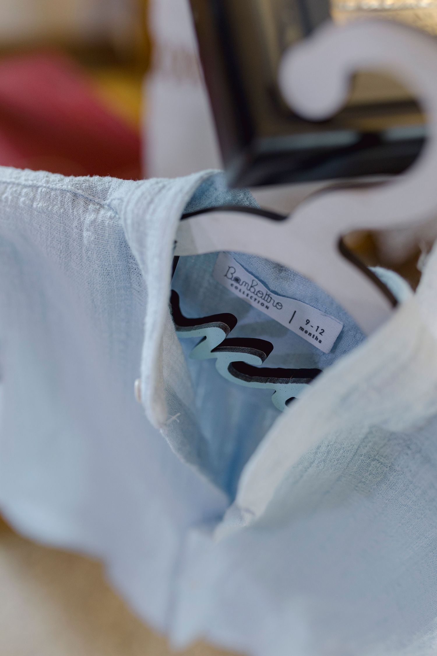 Light blue baby shirt on a hanger with a size 9-12 months label visible inside the collar.