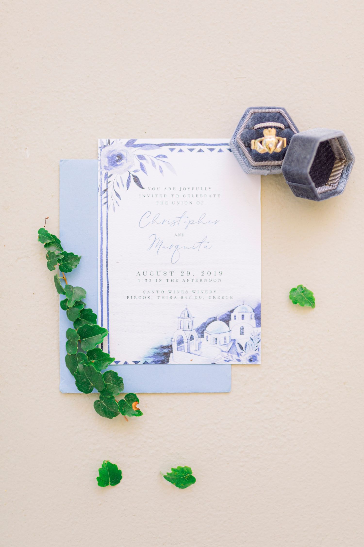 Blue watercolor wedding invitation suite with greenery and a velvet ring box on a neutral background.
