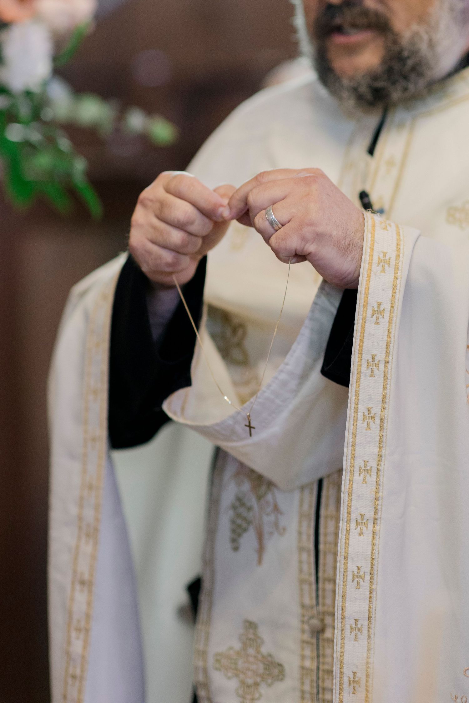 Orthodox priest in white vestments with gold cross embroidery holds a ceremonial item during a religious service.