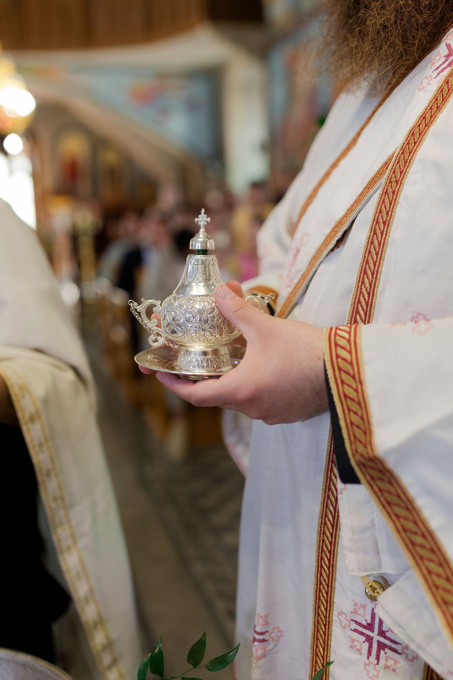 Orthodox priest in white vestments holding ornate silver incense burner during religious ceremony.