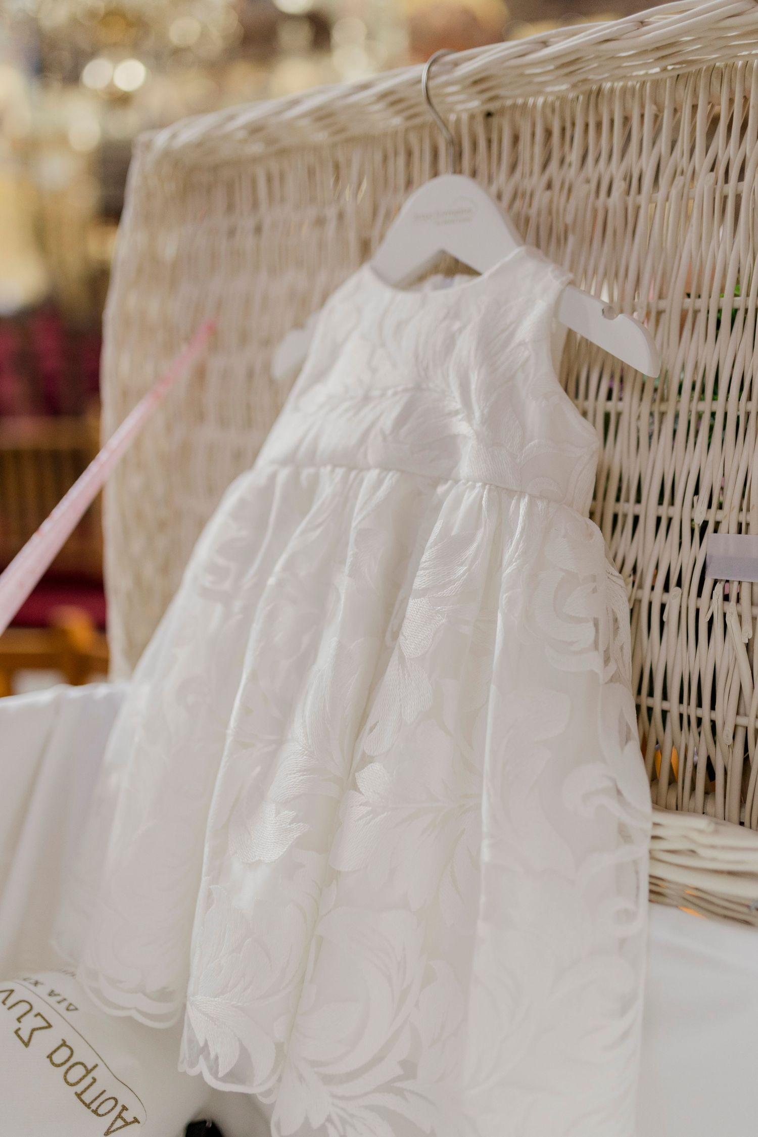 White embroidered baby dress on hanger displayed against wicker basket, perfect for christening or special occasion.