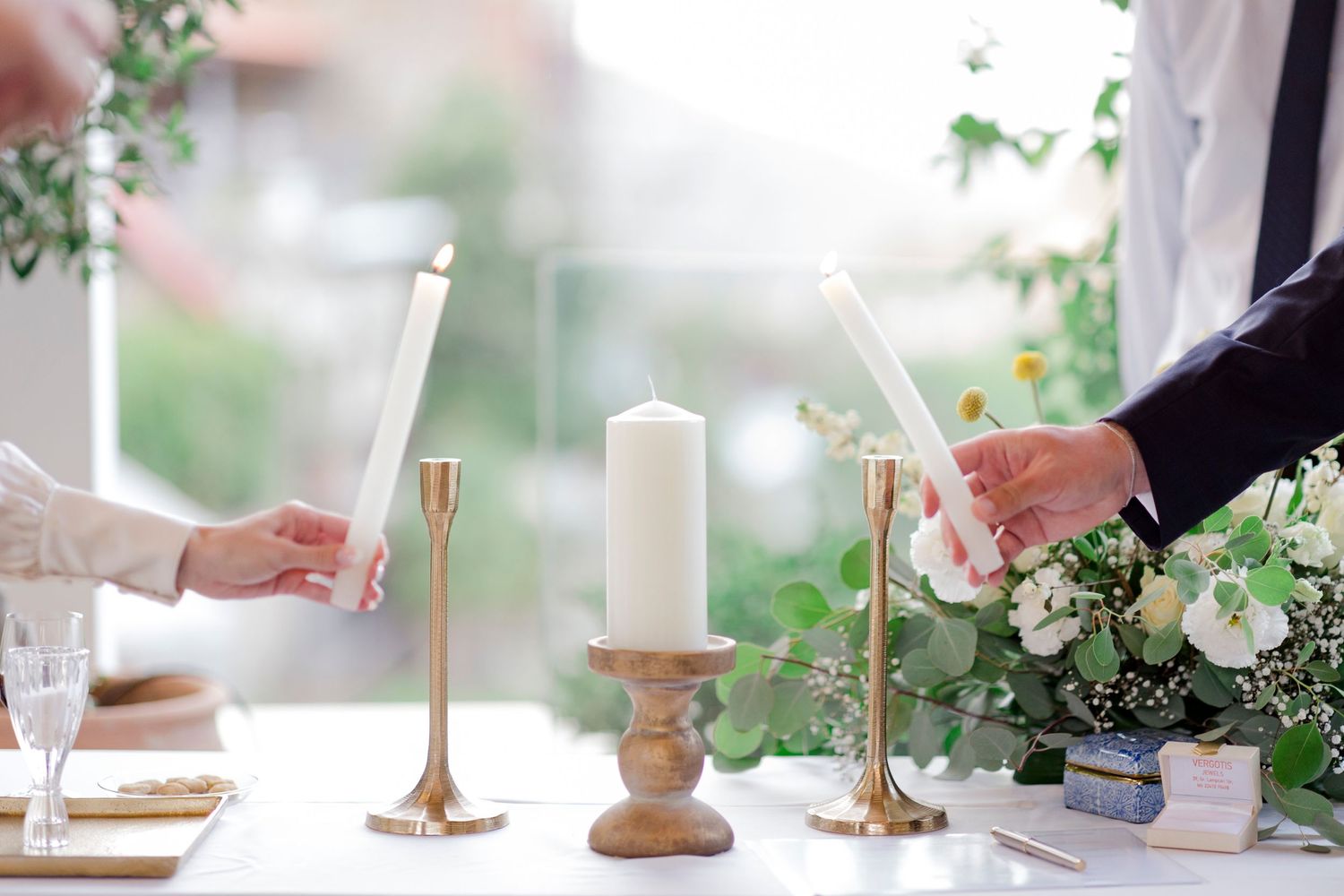 Unity candle ceremony with gold candleholders and white pillar candle on decorated wedding altar table.