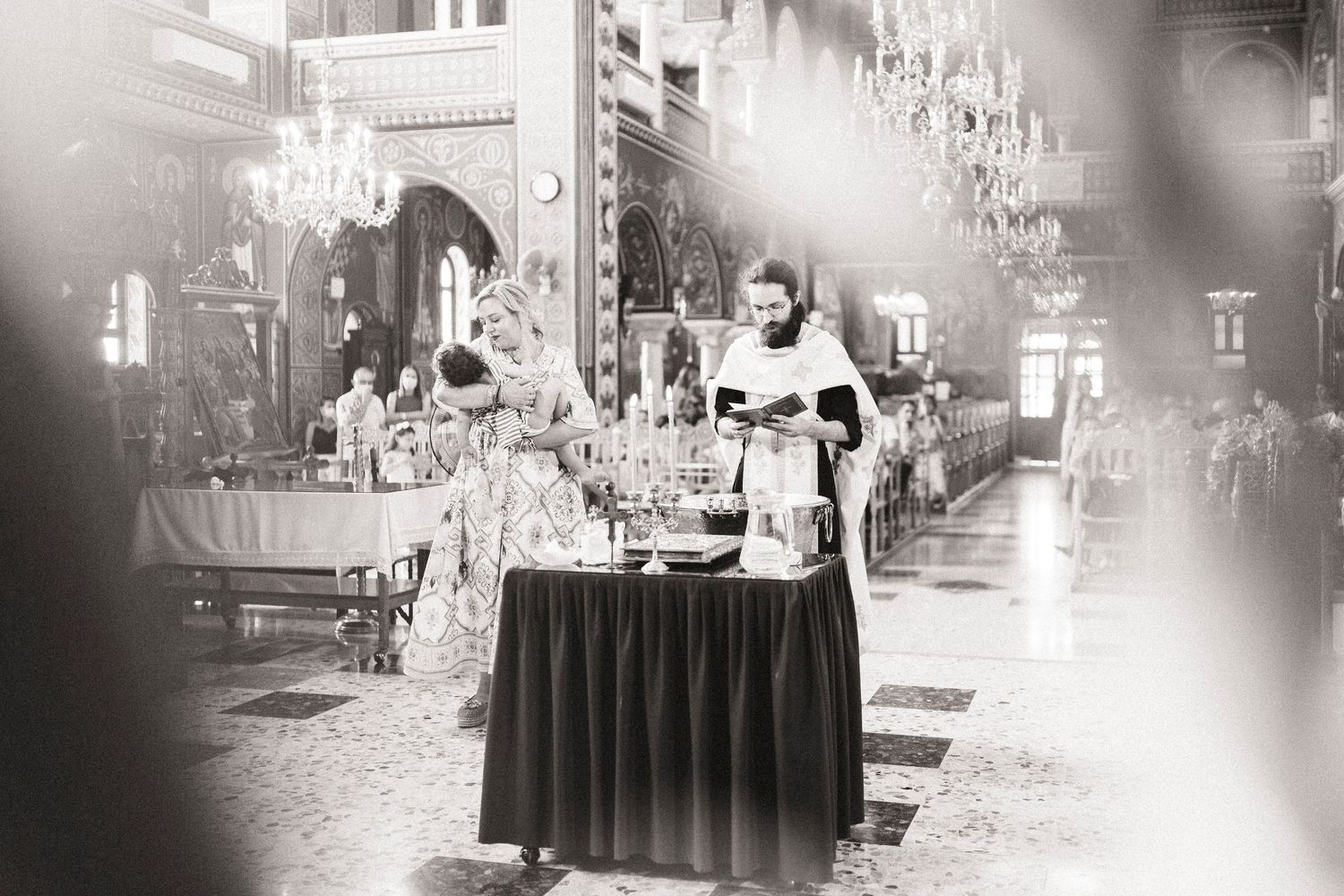 Black and white photo of clergy performing a religious ceremony at an ornate church altar with chandeliers.