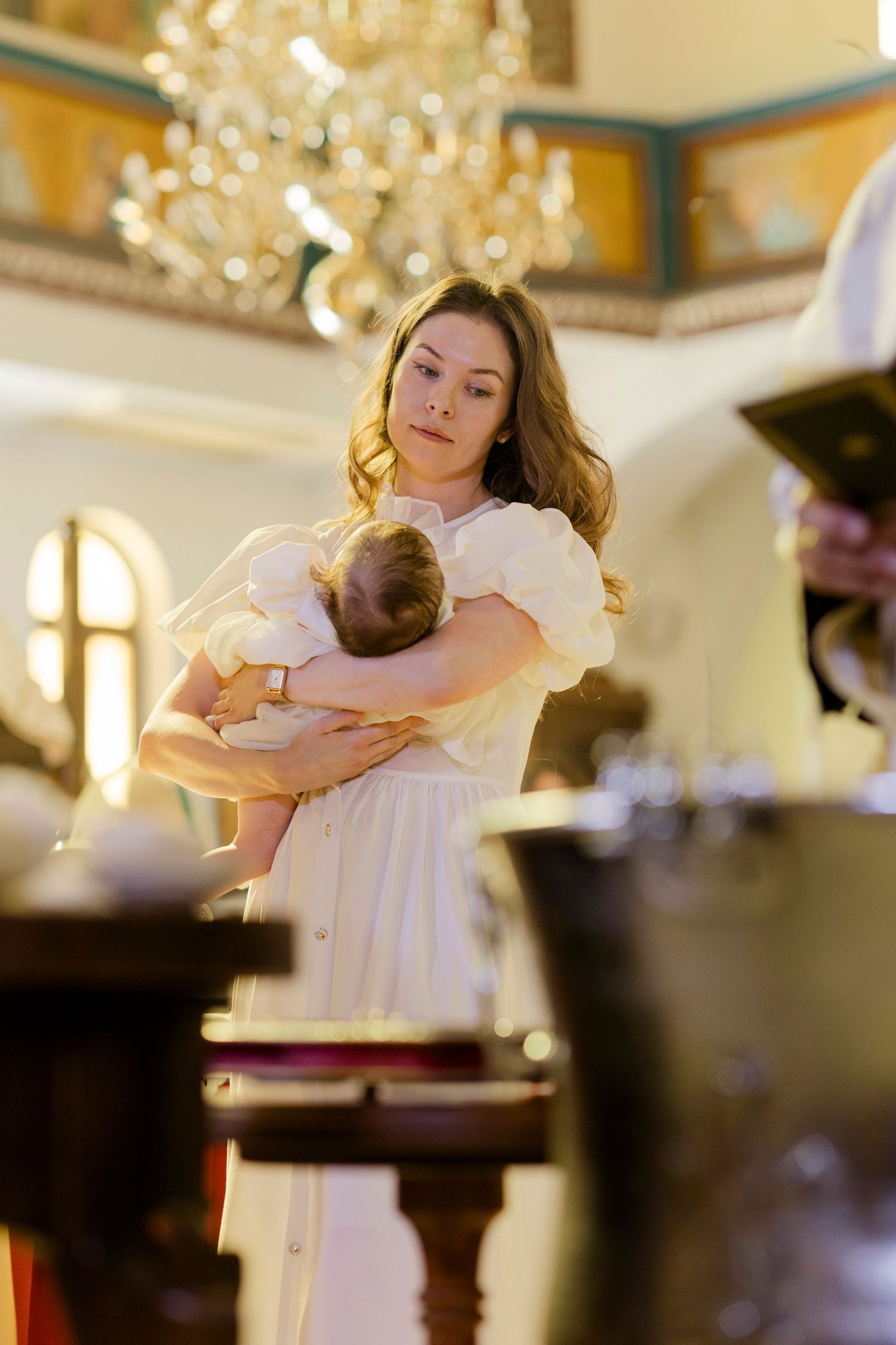 A young woman in a white dress holds a baby during a church baptism ceremony.