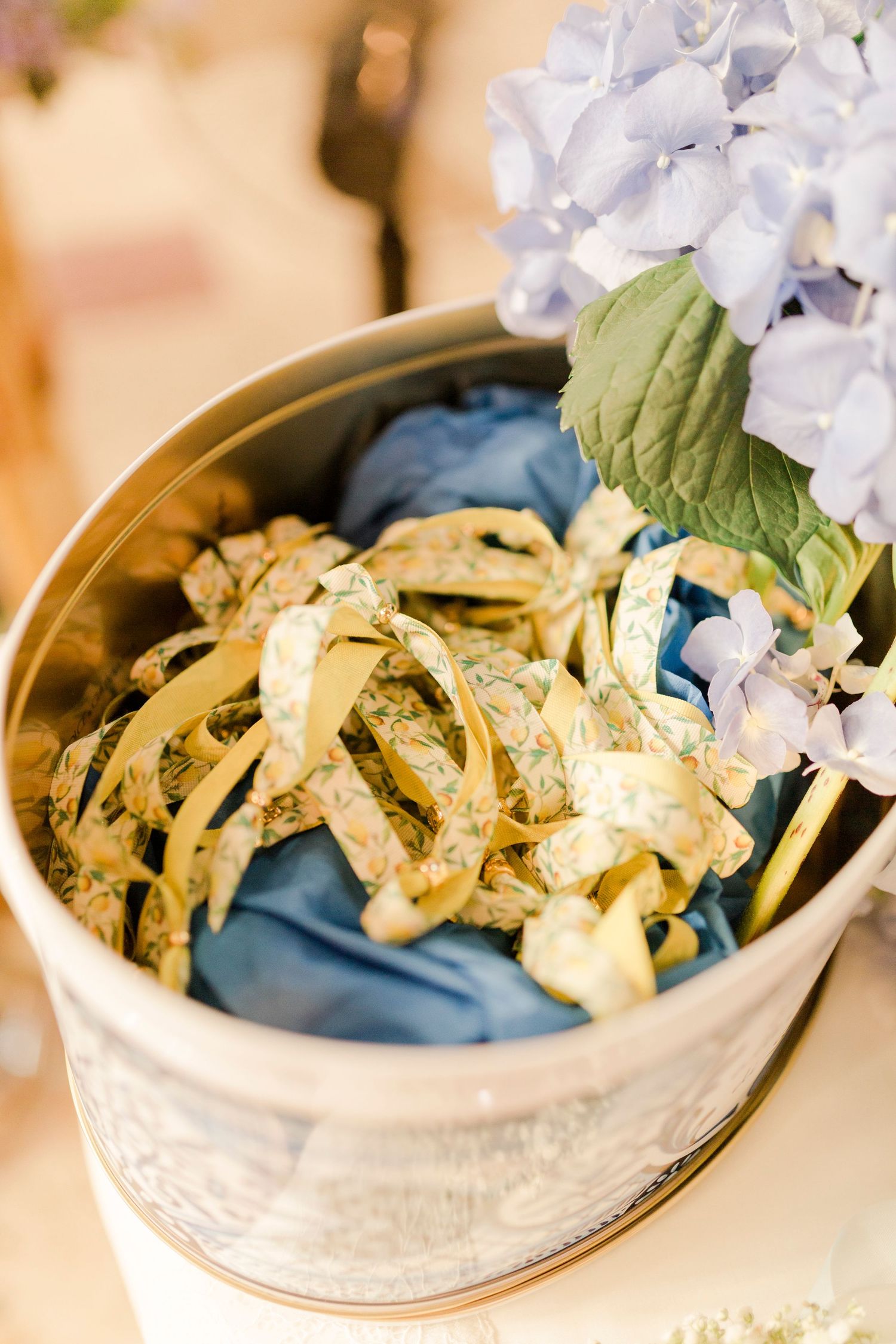 Silver bucket with blue hydrangeas and gold ribbon bows, elegant wedding decor centerpiece arrangement.