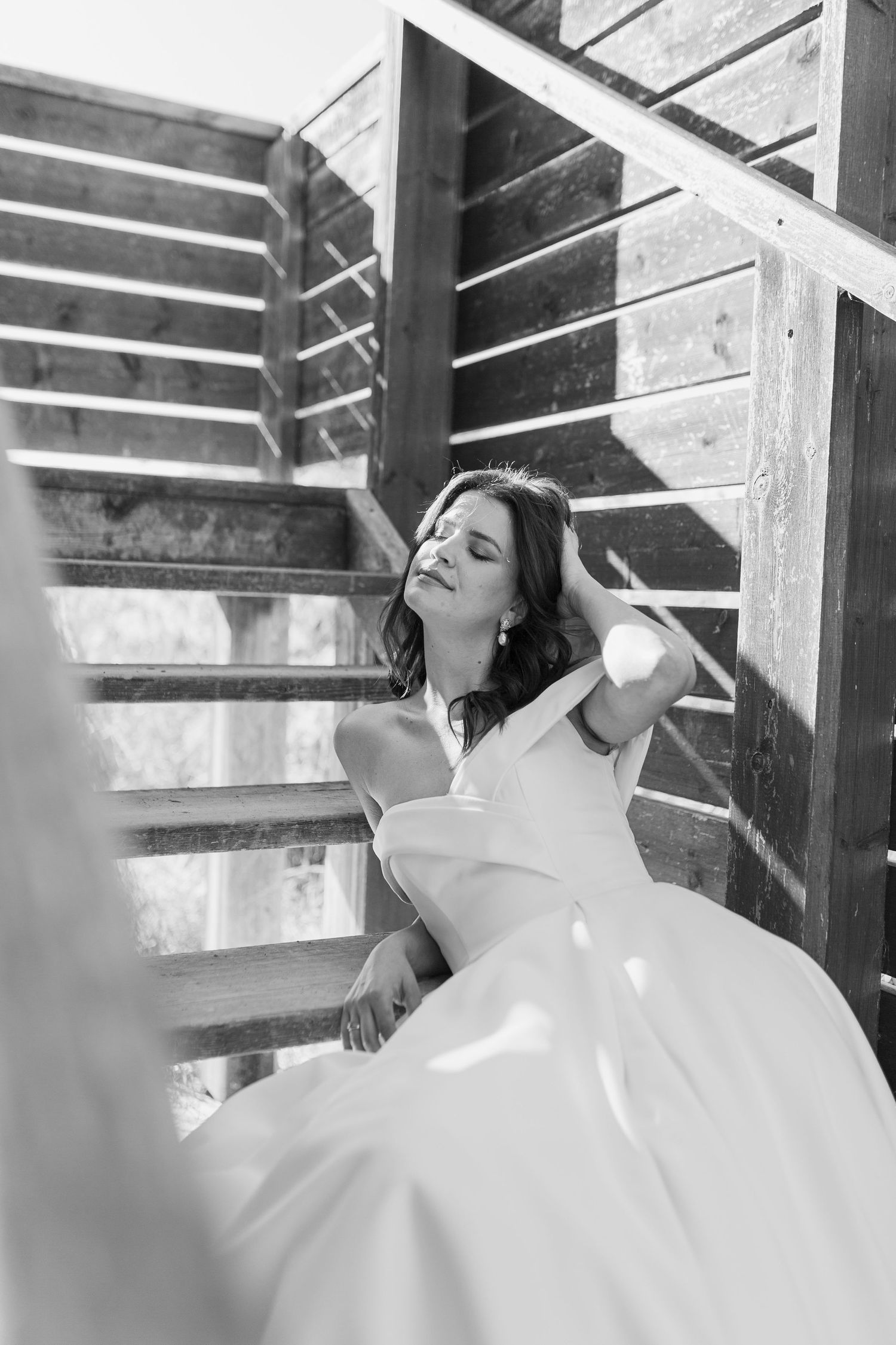 Black and white photo of bride in strapless gown posing gracefully on wooden outdoor staircase.