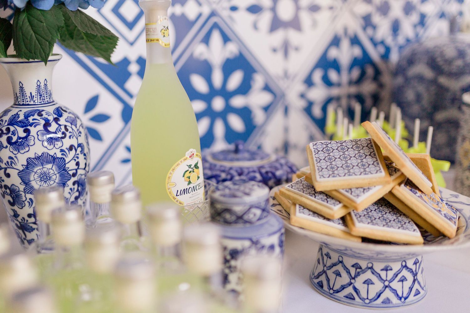 Blue and white themed dessert table with lemon cookies, limoncello bottle, and decorative tiles.