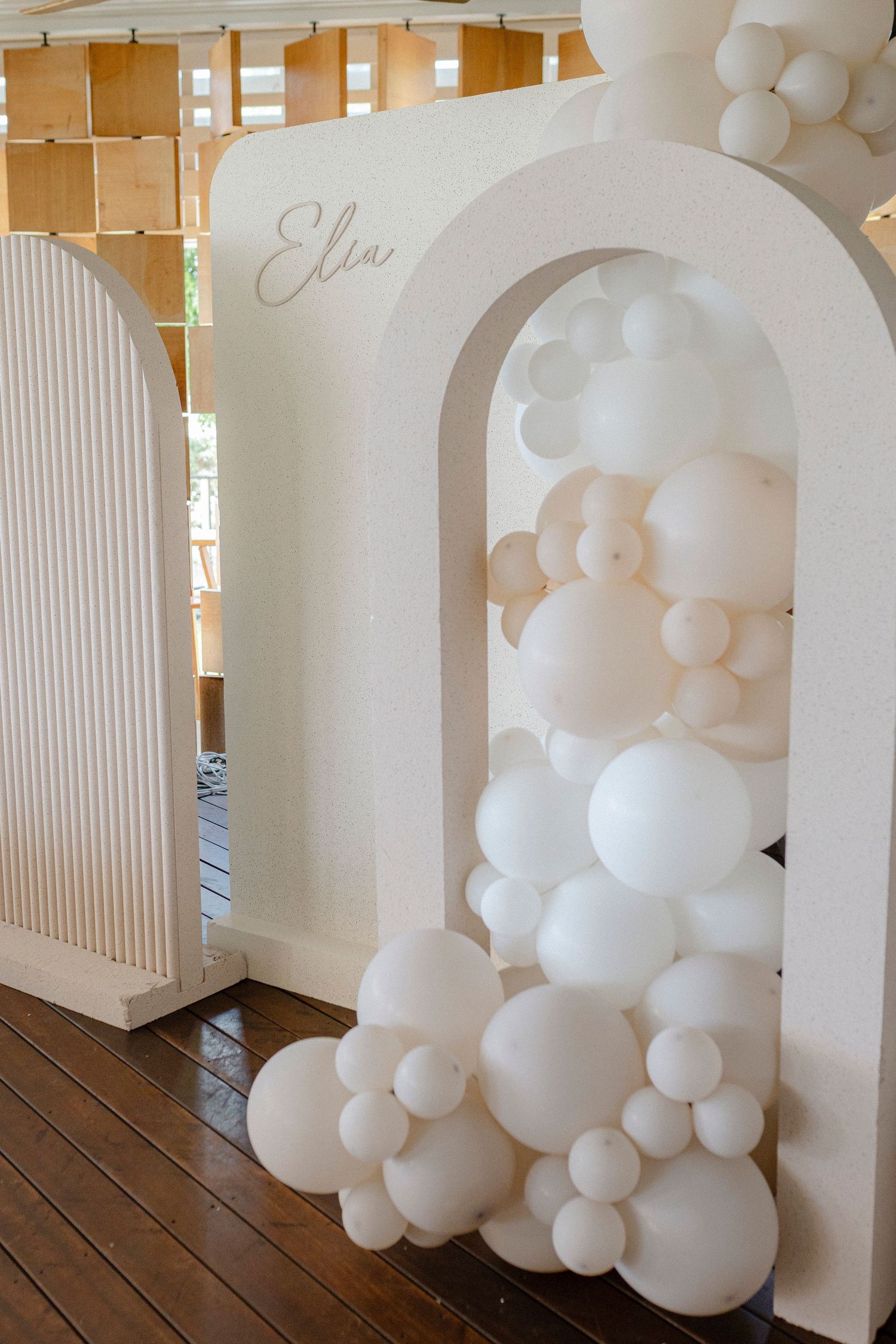Elegant white arch backdrop with balloon garland display featuring ivory and beige balloons for a party event.