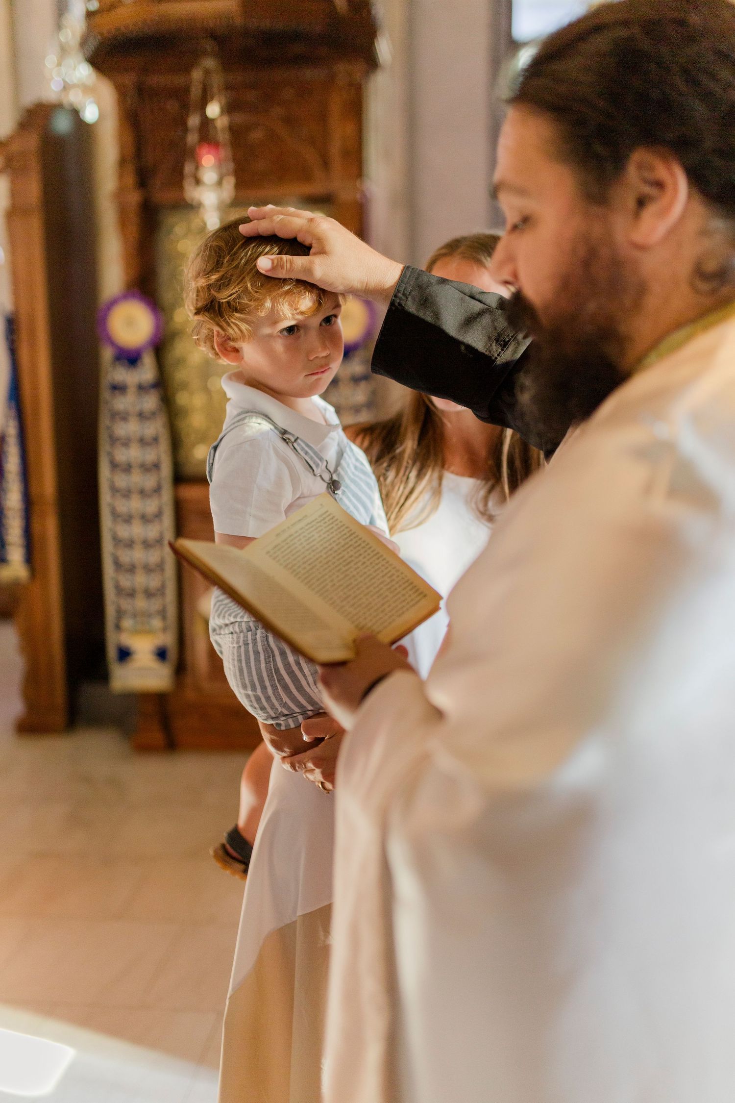 Priest blessing a young child during a baptism ceremony in a church, holding a holy book.