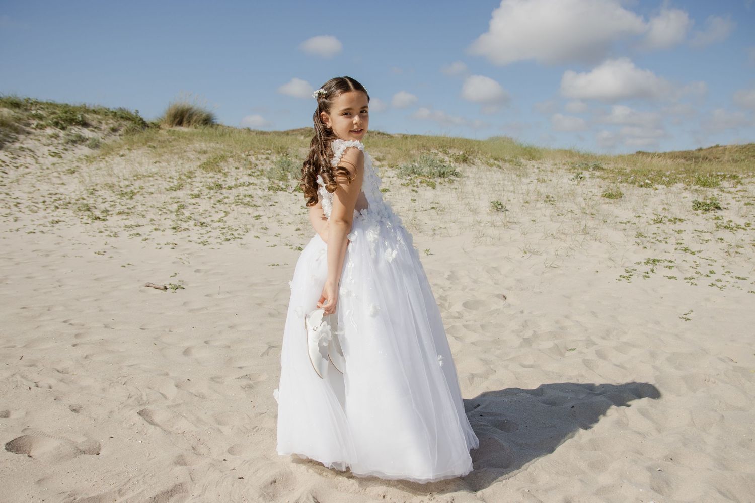 Menina de vestido branco na praia a segurar nos sapatos de comunhão, atrás das costas. Vila do Conde, Azurara