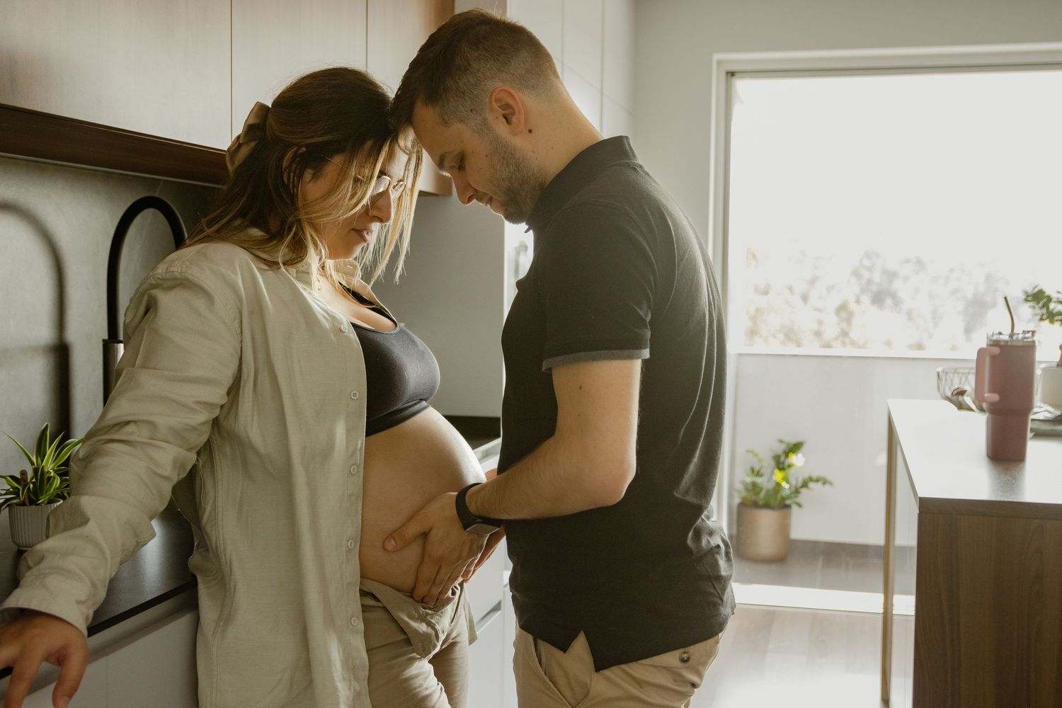 Fotografia de gravidez. Pais na cozinha. Pai com as mãos na barriga com grávida. descontraido. Maia