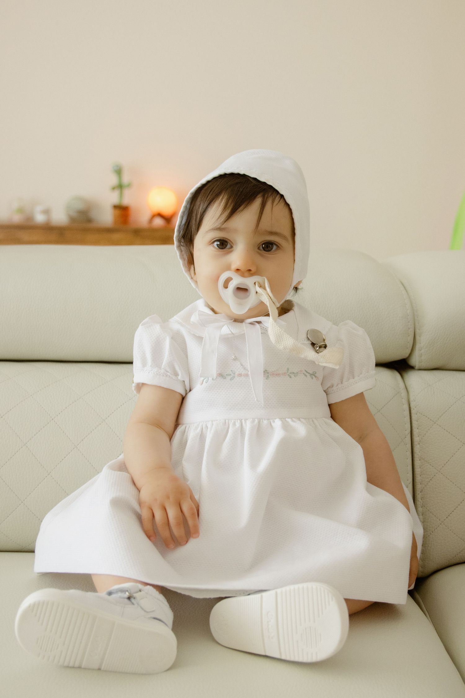 Fotografia de batizado. Bebé sentada no sofá em casa. Maia