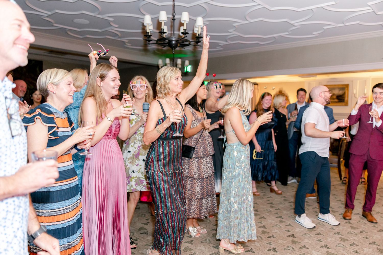 Wedding guests dance in a line following choreographed moves at a reception party with pink lighting.