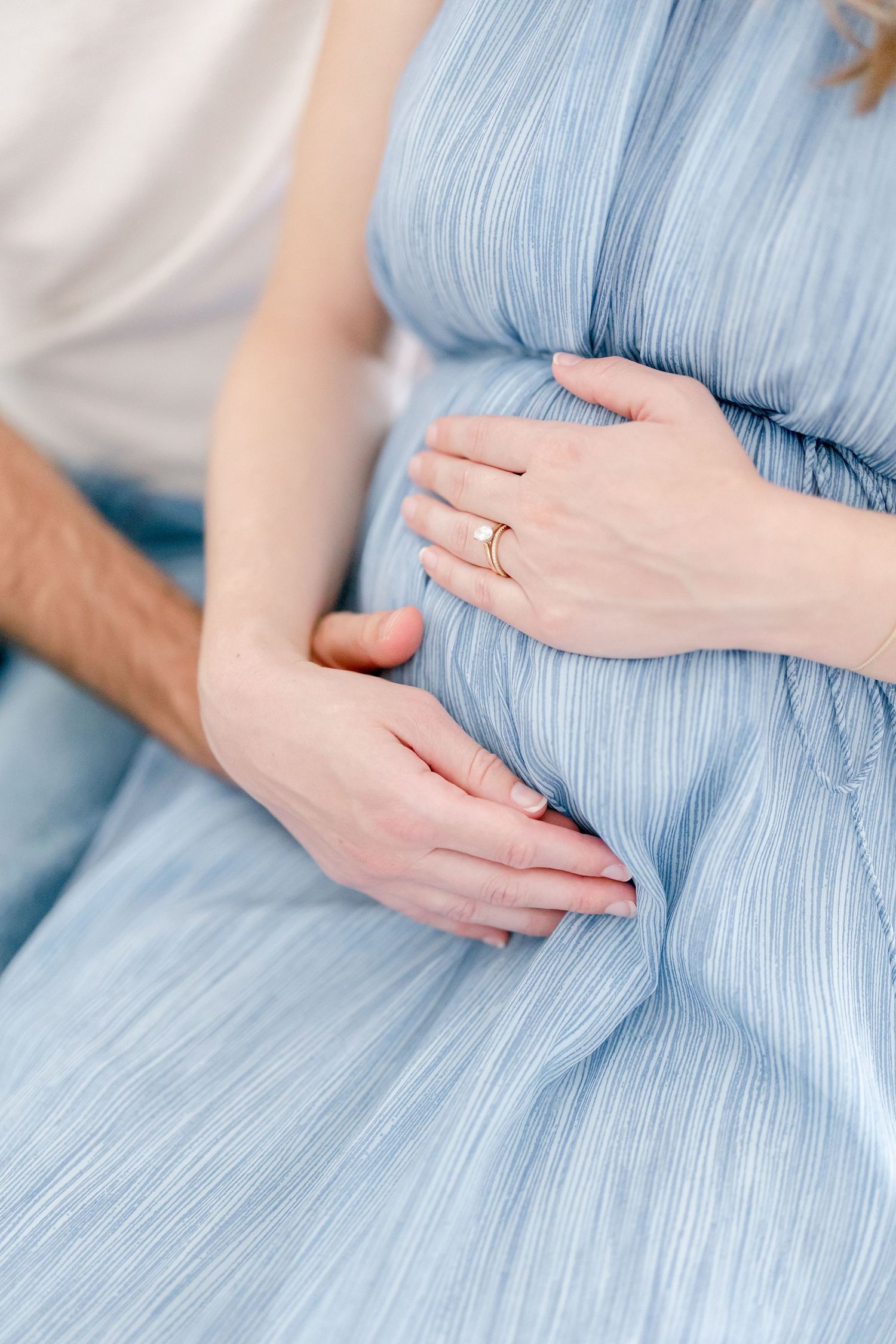 Close up of hands tenderly resting on light blue maternity dress showing baby bump.