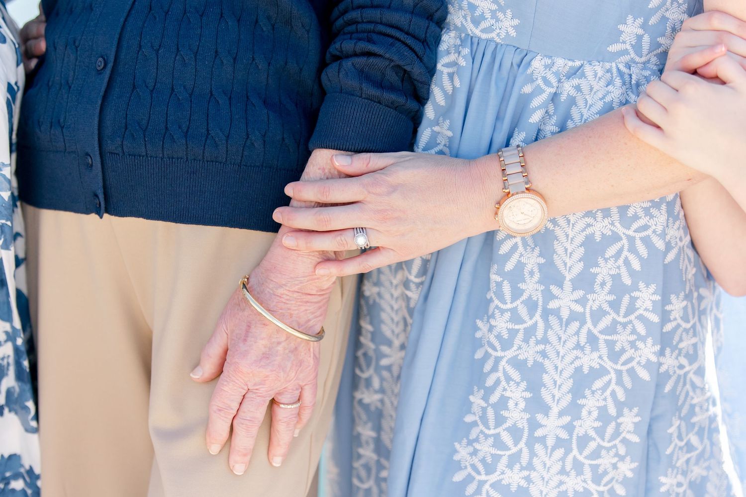 Close-up of hands with engagement ring showing between two people wearing navy and light blue clothing.