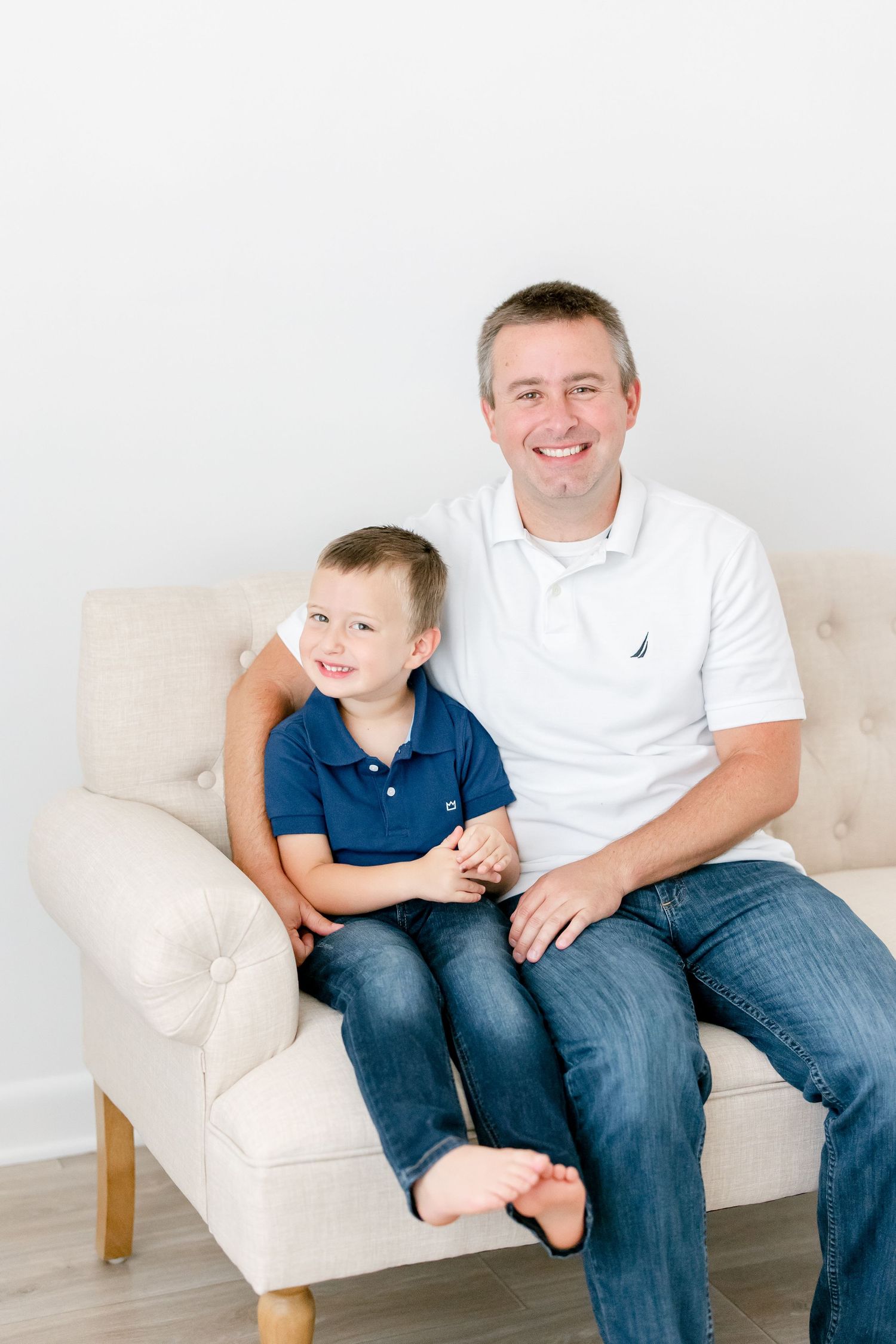 Parent and child wearing blue and white shirts sitting together on beige sofa.