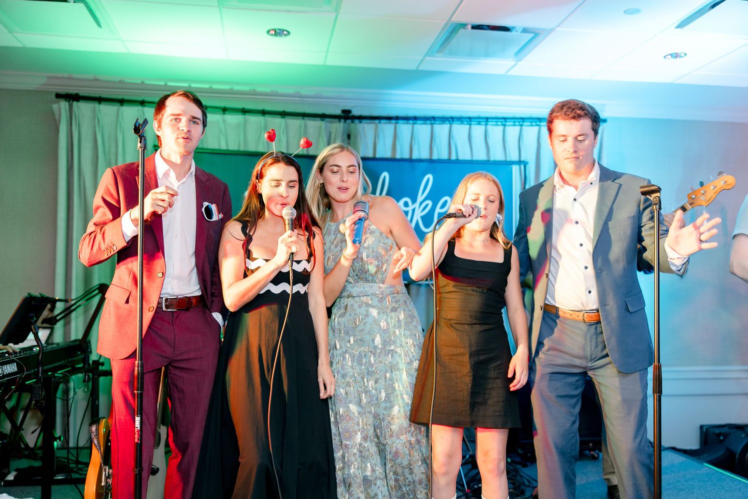 Group of party guests singing and celebrating together under colored lighting at evening event.